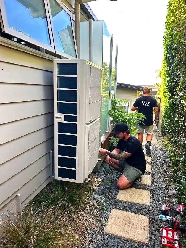 Volt Solutions electricians  working outside a house, installing or repairing an outdoor air conditioning unit or heat pump beside the house.