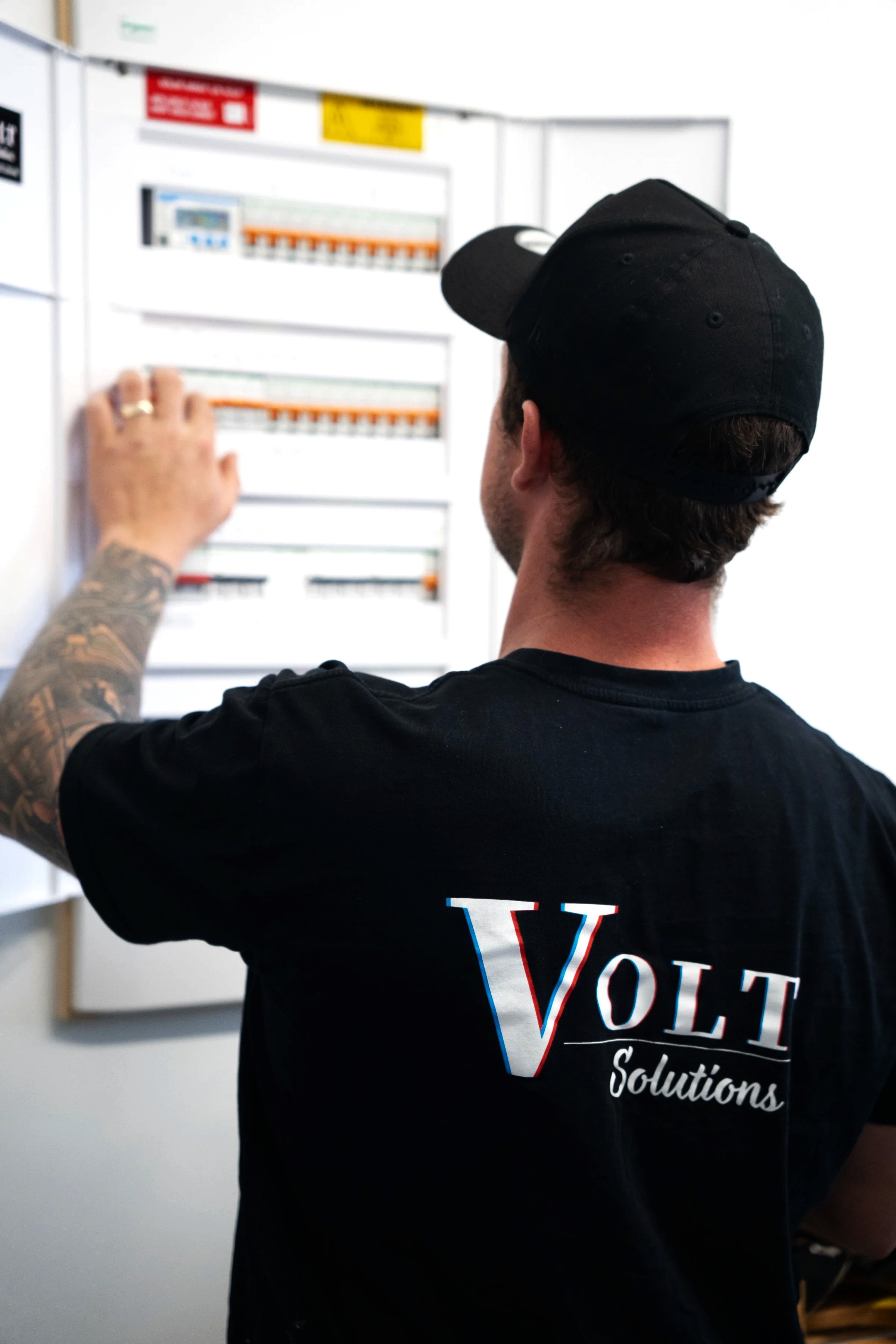 Volt Solutions electrician wearing a black cap and black t-shirt with 'VOLT Solutions' on the back, working on an electrical panel.