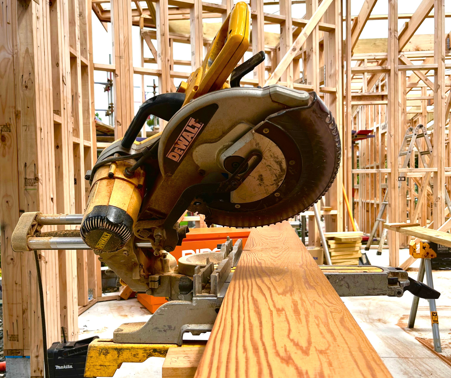 A DeWalt compound miter saw on a workbench in a building under construction, with unfinished wooden framing in the background.  Volt Solutions electrician installed the electrics here. 