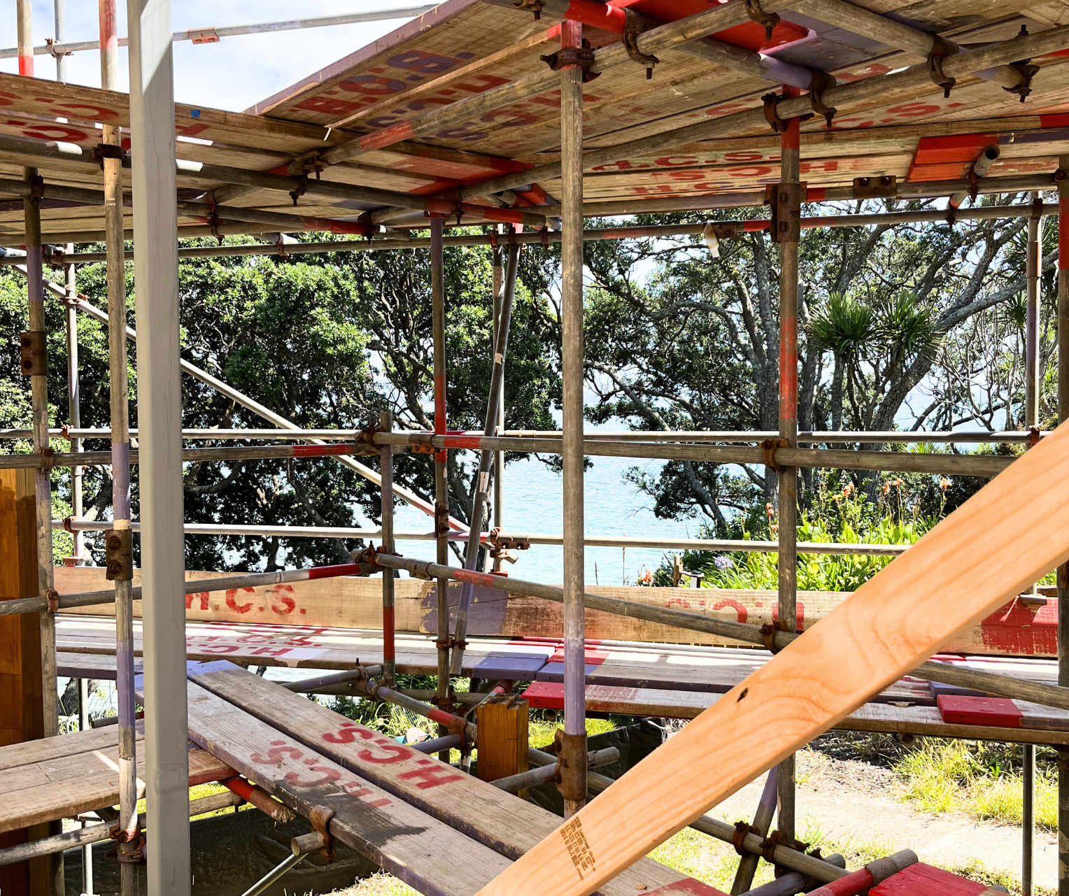 Construction scaffolding with wooden planks and a view of trees and water in the background.