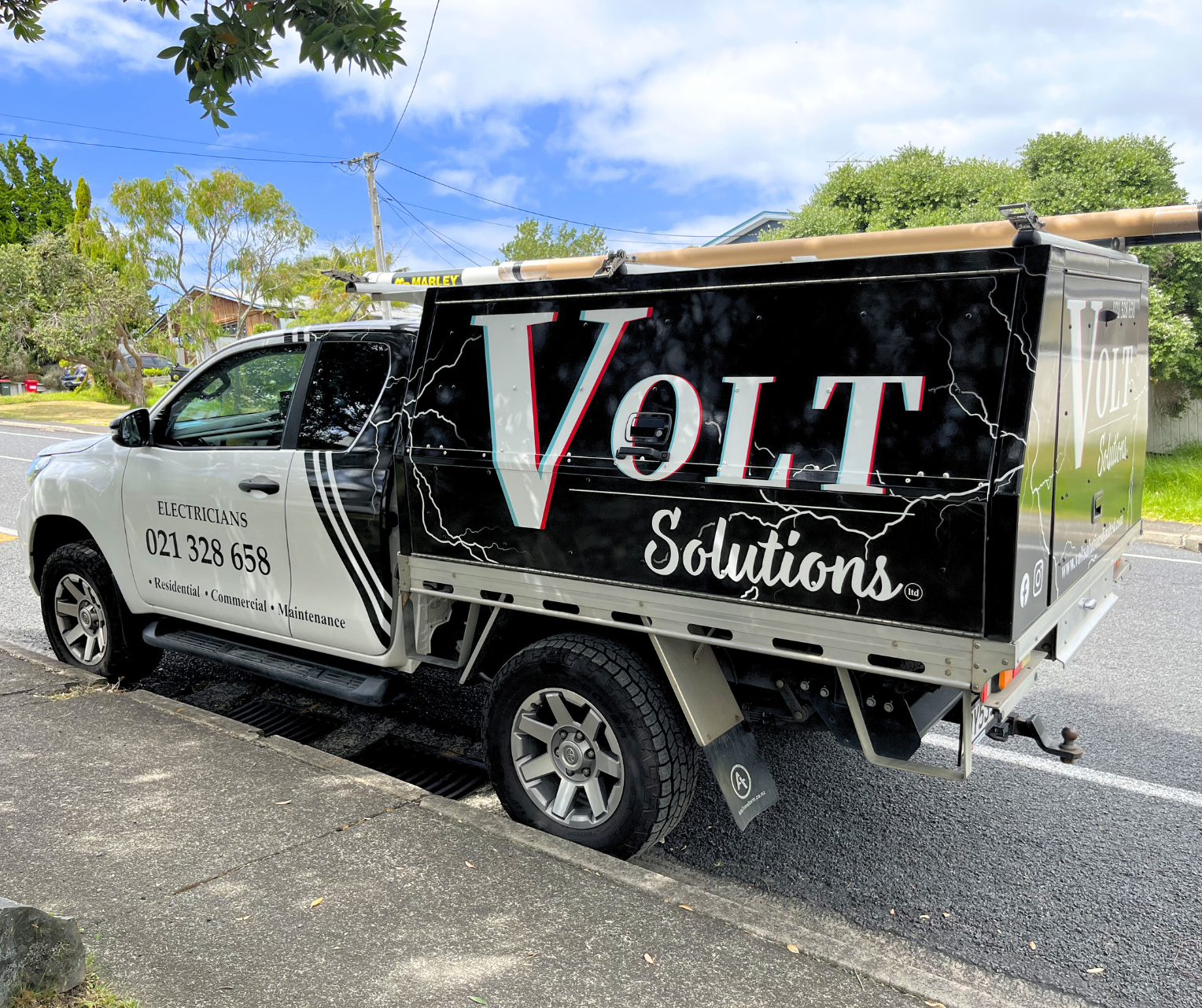 Electrician truck parked on the street with advertising for Volt Solutions, featuring lightning bolt graphics and contact information.