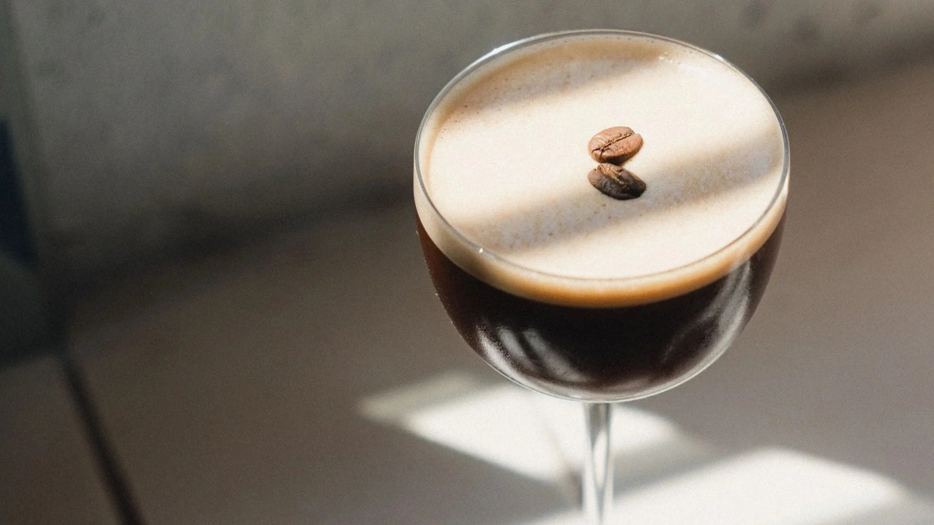 A cocktail glass filled with a dark beverage topped with foam and garnished with two coffee beans.