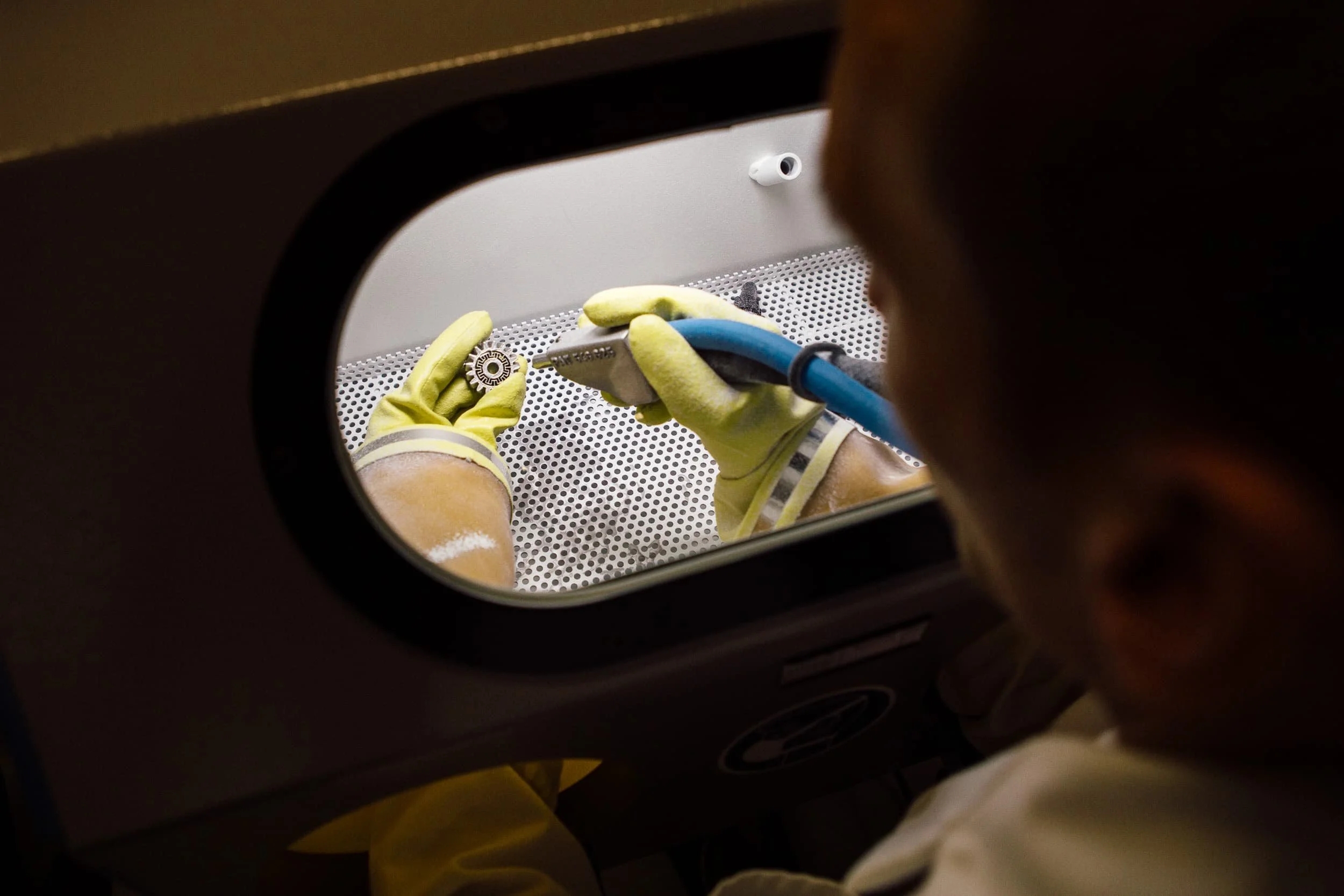 Eine Person trägt Handschuhe und bedient eine Maschine, die wahrscheinlich medizinisches Equipment verarbeitet, durch eine runde Öffnung im Blickfeld.