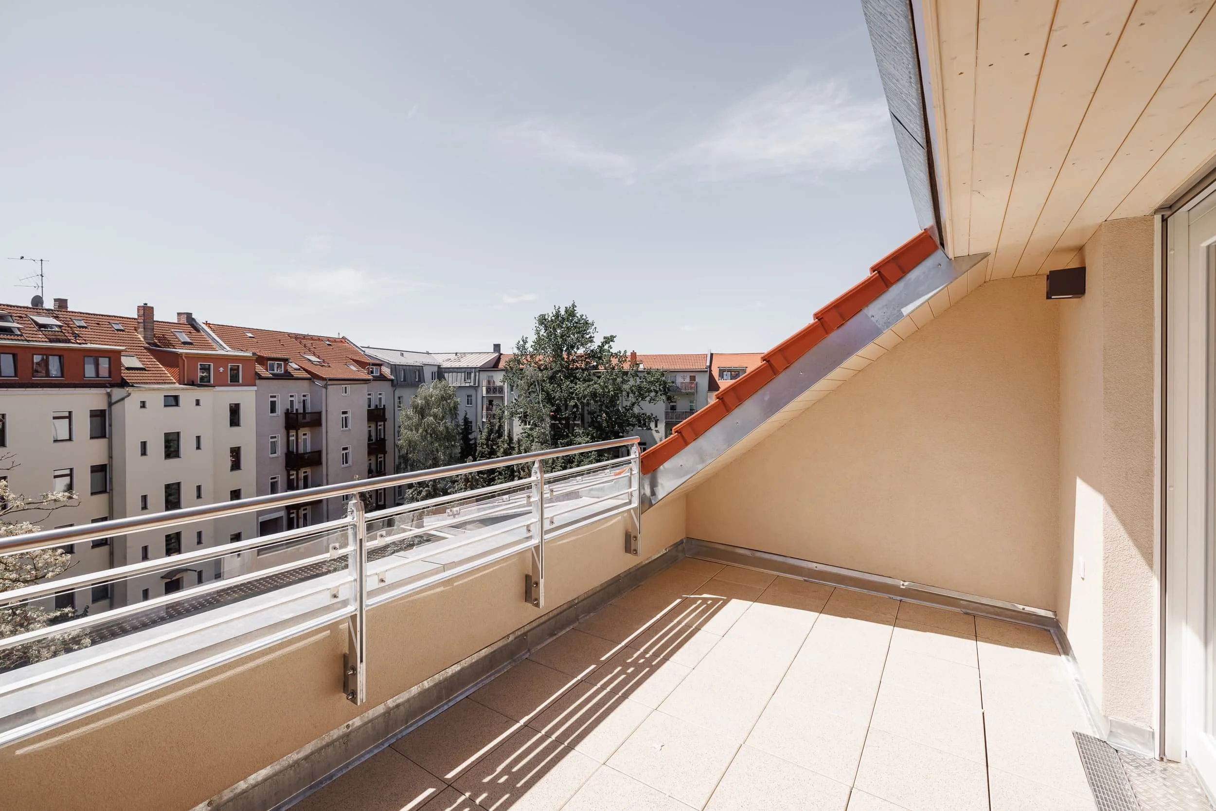 Balkon mit weißem Geländer, Blick auf Nachbarhäuser mit roten Ziegeldächern und blauer Himmel