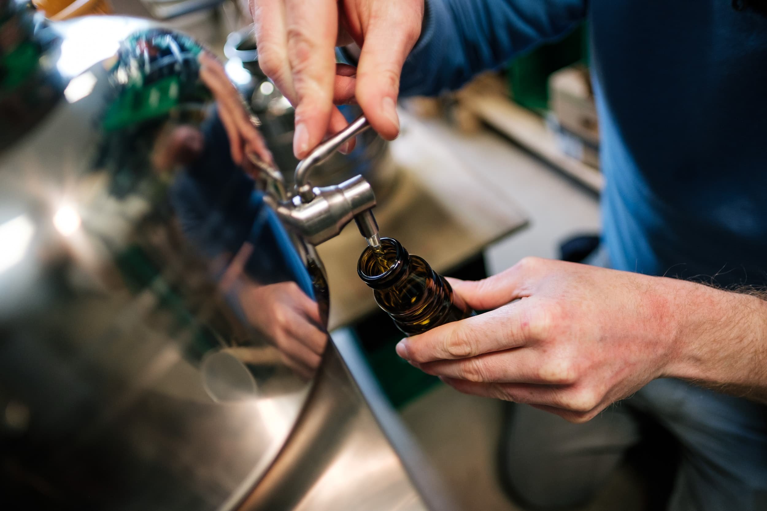 Eine Person gießt Bier aus einem Flaschenöffner in eine braune Flasche.