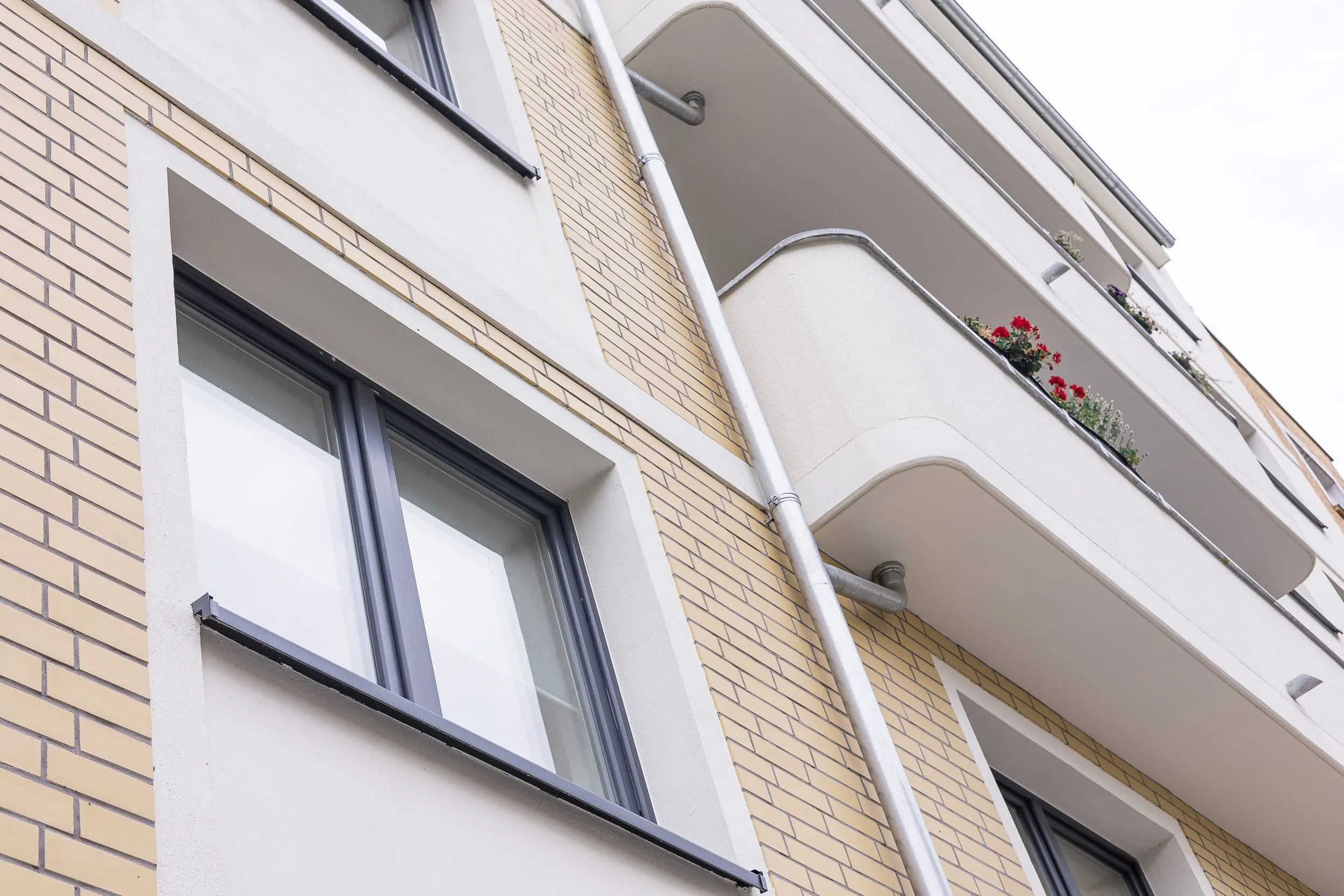 Ansicht eines mehrstöckigen Apartmentgebäudes mit Balkonen, Zierpflanzen und einem Wasserablaufrohr.