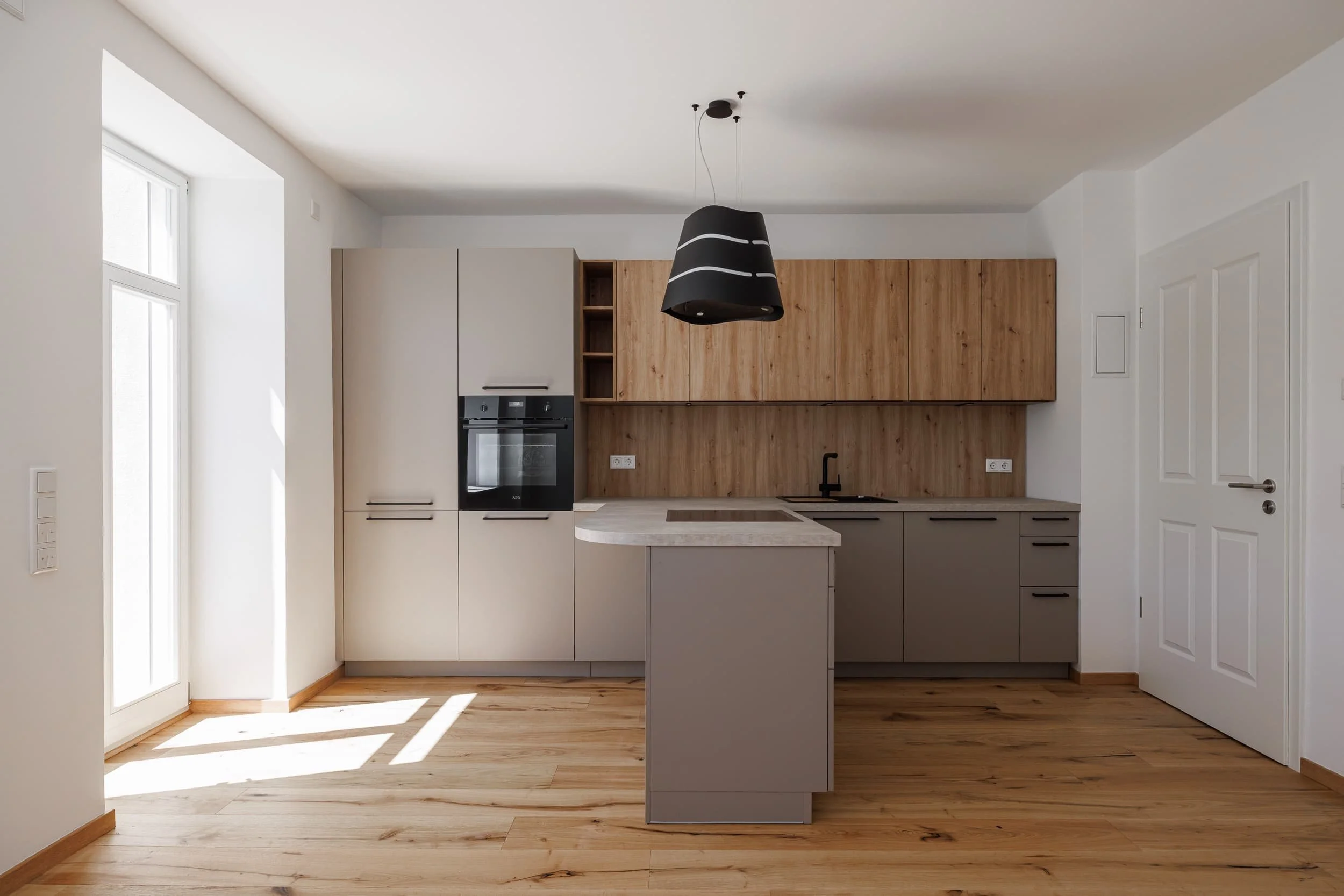 Moderne Küche mit weißen und Holzschränken, schwarzen Armaturen, Herd und Dunstabzug, Naturholzboden und viel natürlichem Licht von Glasfenstern.