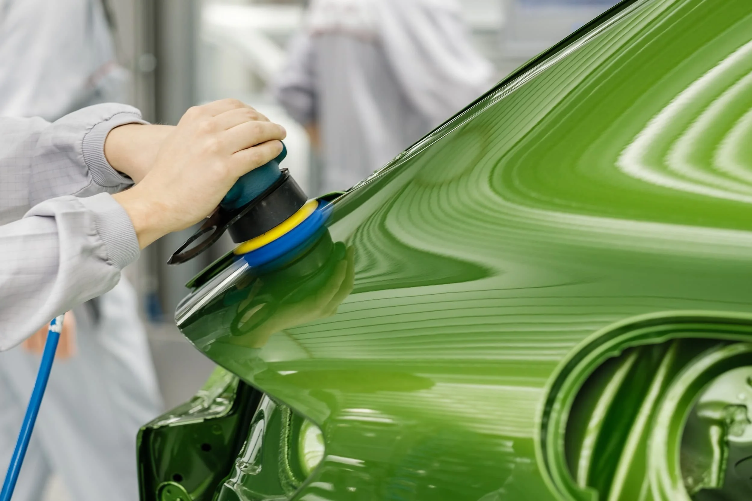 Ein Auto wird in einer Werkstatt poliert, mit einem Handgerät und mehreren Polierpads, während das Auto eine grüne Lackierung hat.