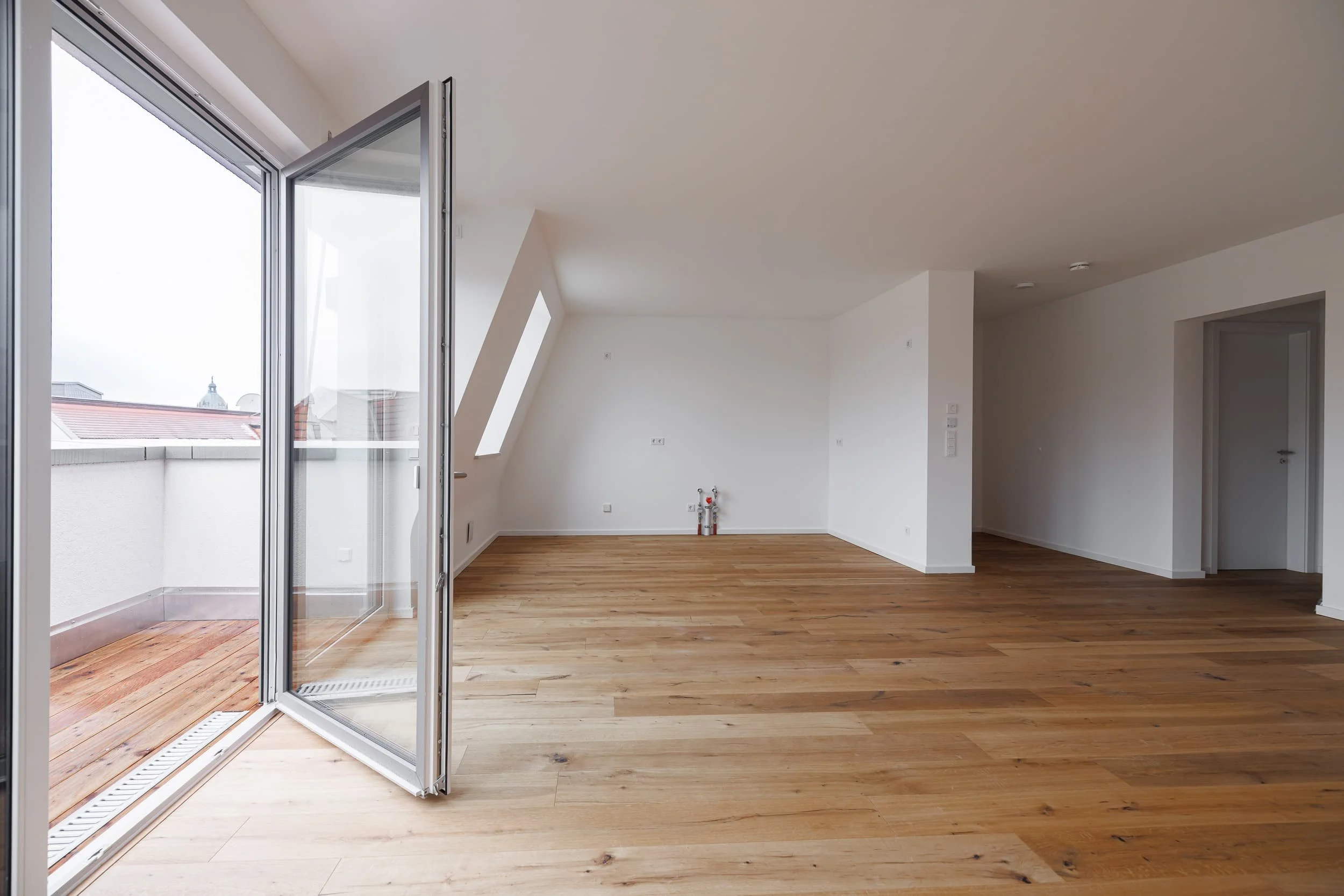Leeres, helles Zimmer mit großen Fenstern und Holzboden, Balkon zu sehen.