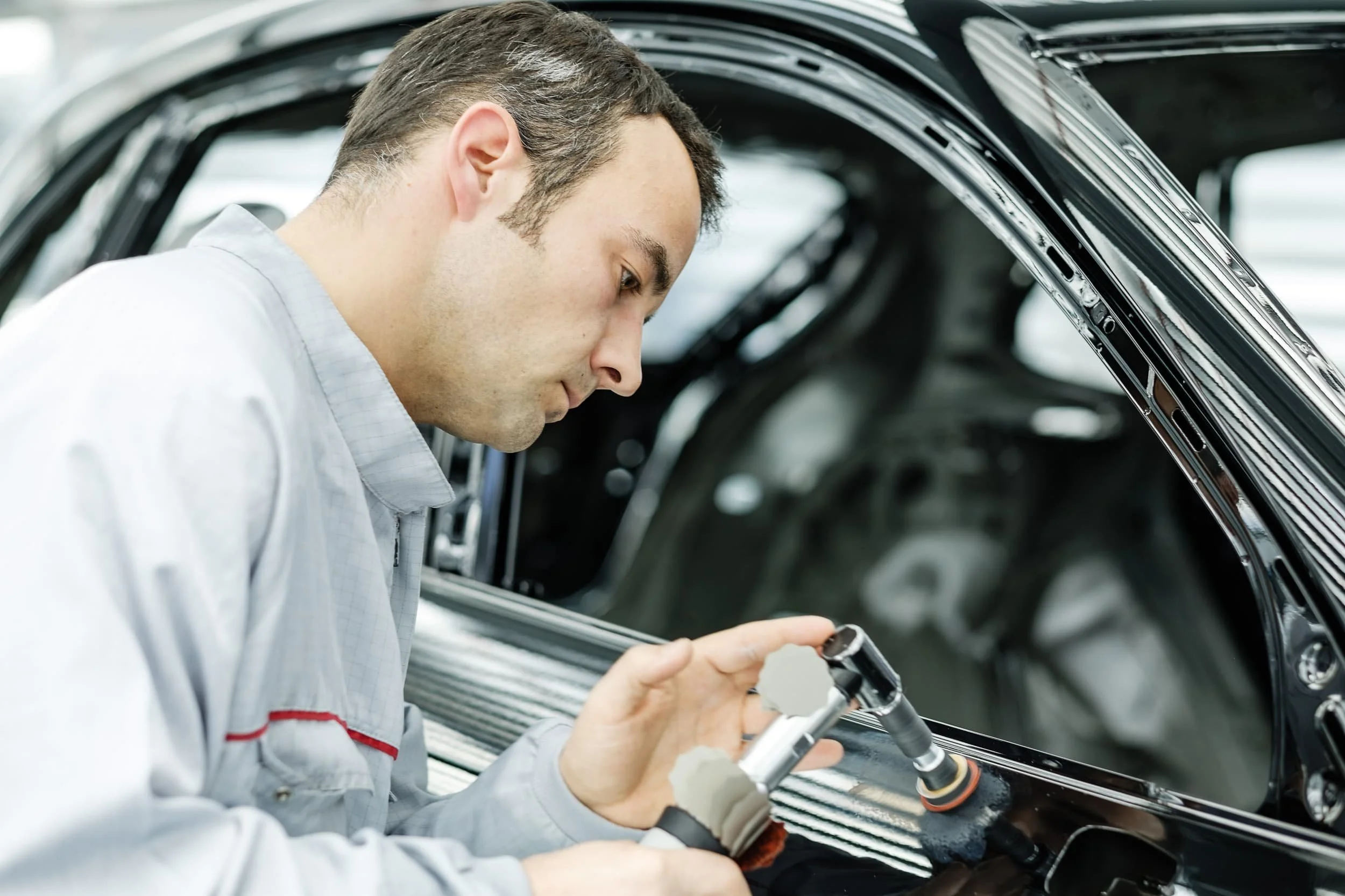 Ein Mann arbeitet an einer Autotür im Werkstatt- oder Montagebereich.