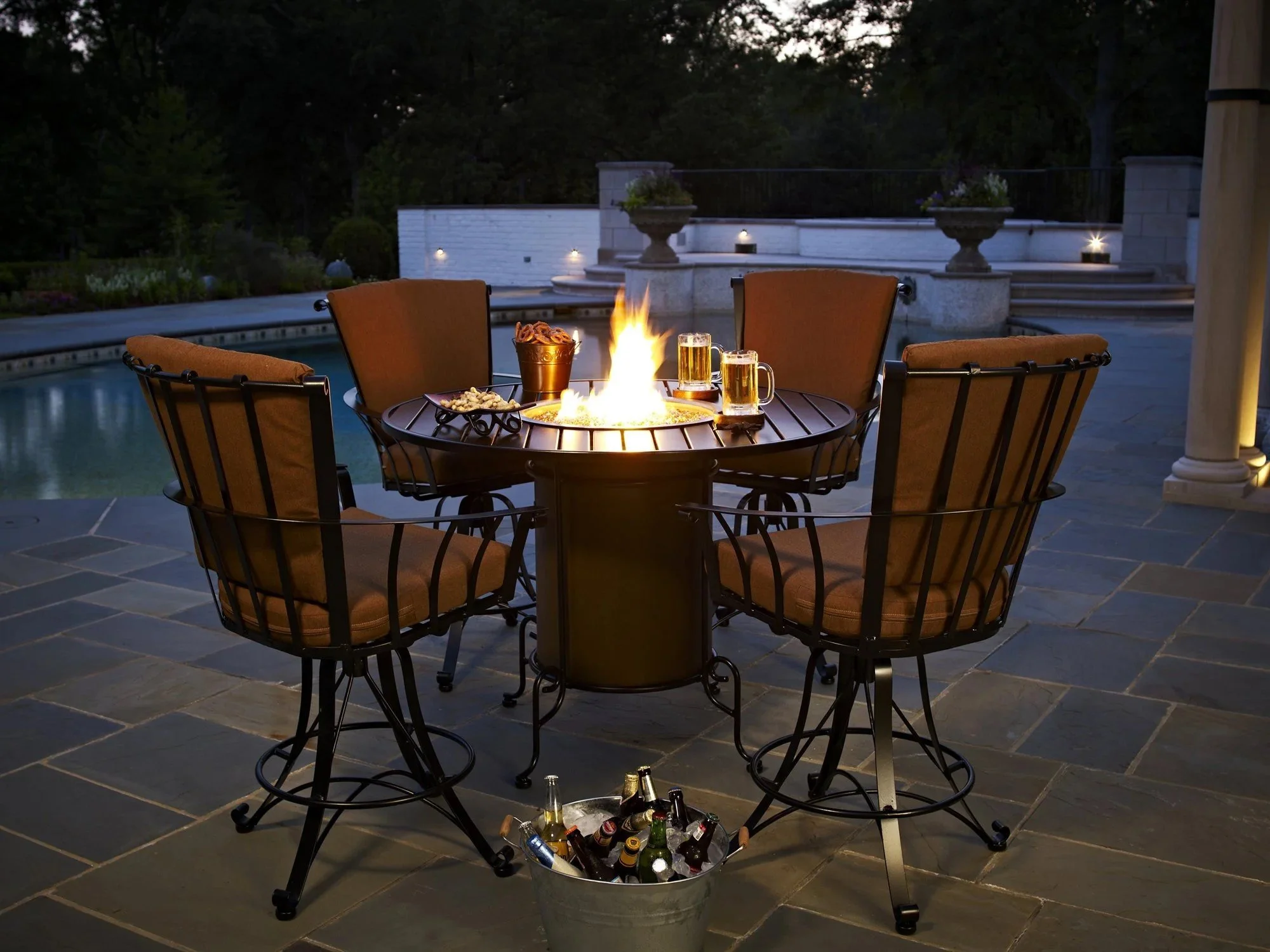 Four wrought iron high top chairs with brown cushions around fire table on tiled hardscape