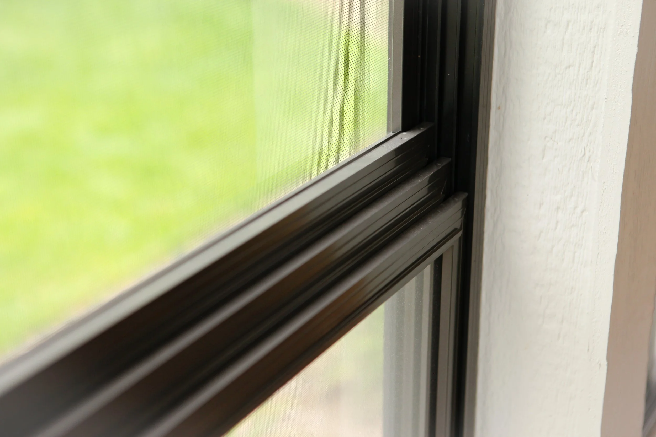 Close-up of a black window screen frame with a mesh screen, next to a white wall.
