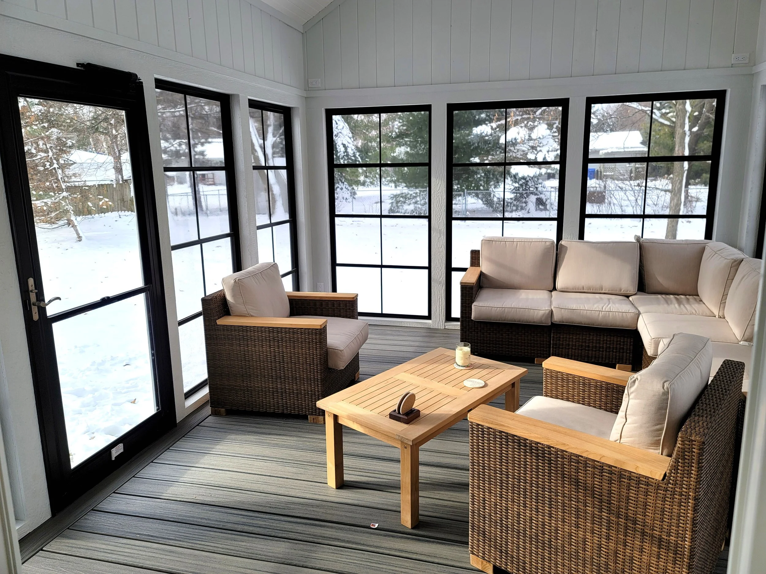 Sunroom with wicker furniture and large windows showing snowy outdoor landscape.