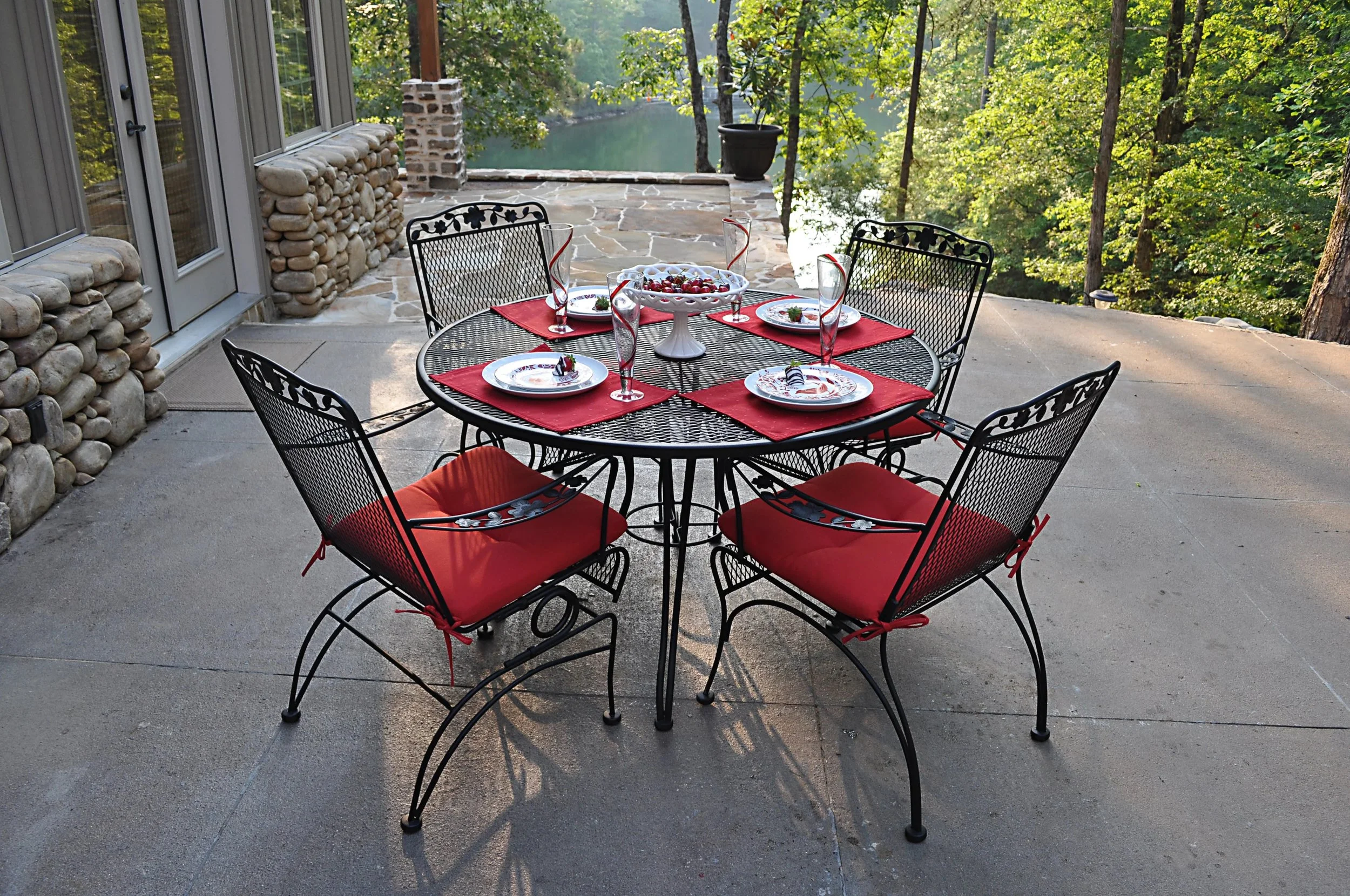 5 piece wrought iron dining set with red sushions on hardscape porch looking over water and forest