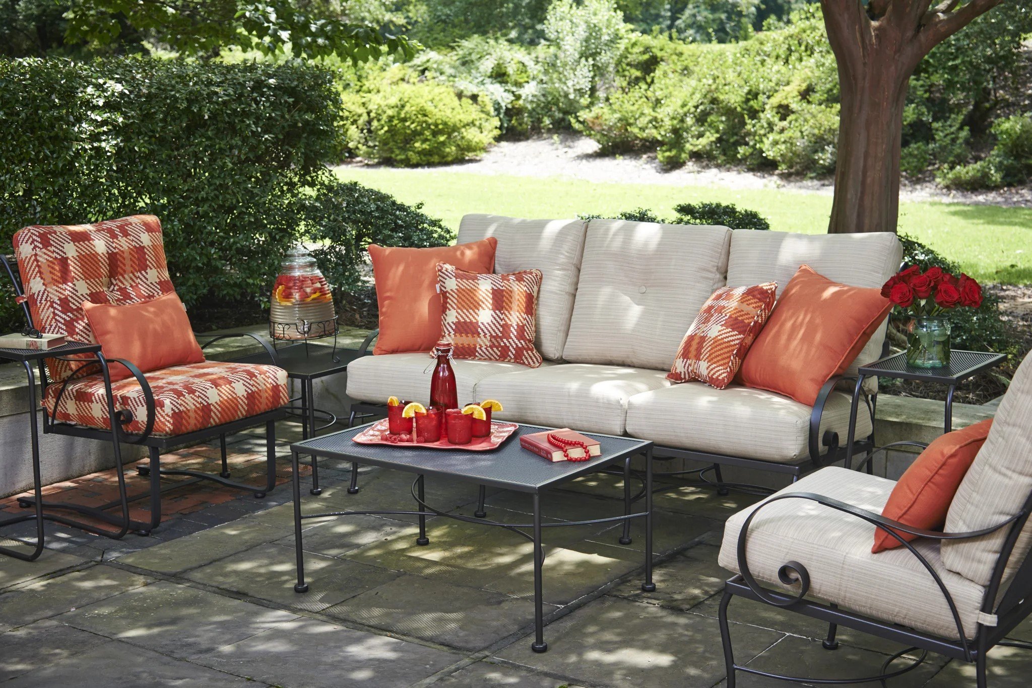 wrought iron lounge set with beige or red plaid cushions and red throw pillows on hardscape next to lawn