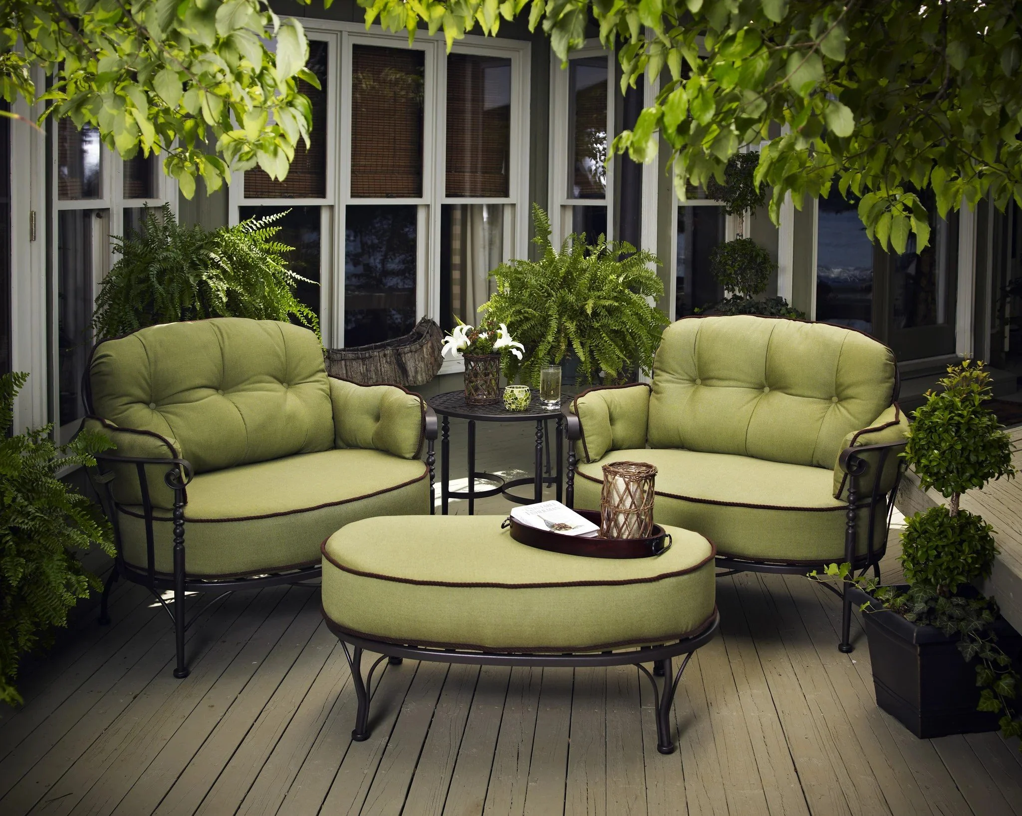 two wrought iron lounge chairs with thick green cushions and matching ottoman with end table on deck surface