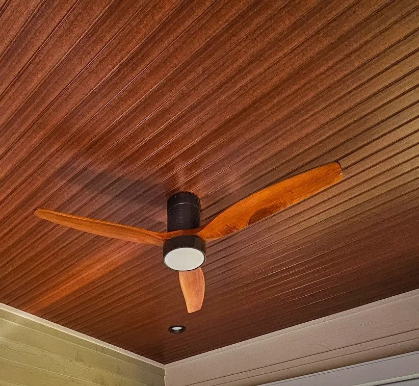 A ceiling fan with three wooden blades mounted on a wooden ceiling.