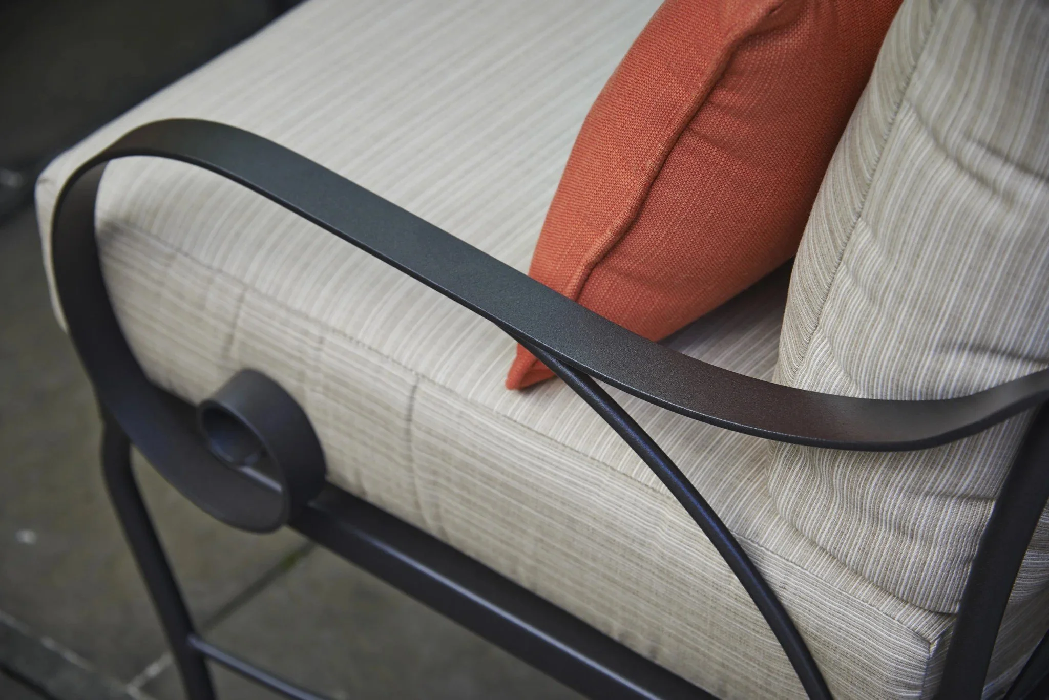close up of wrought iron arm chair with beige cushion and red throw pillow