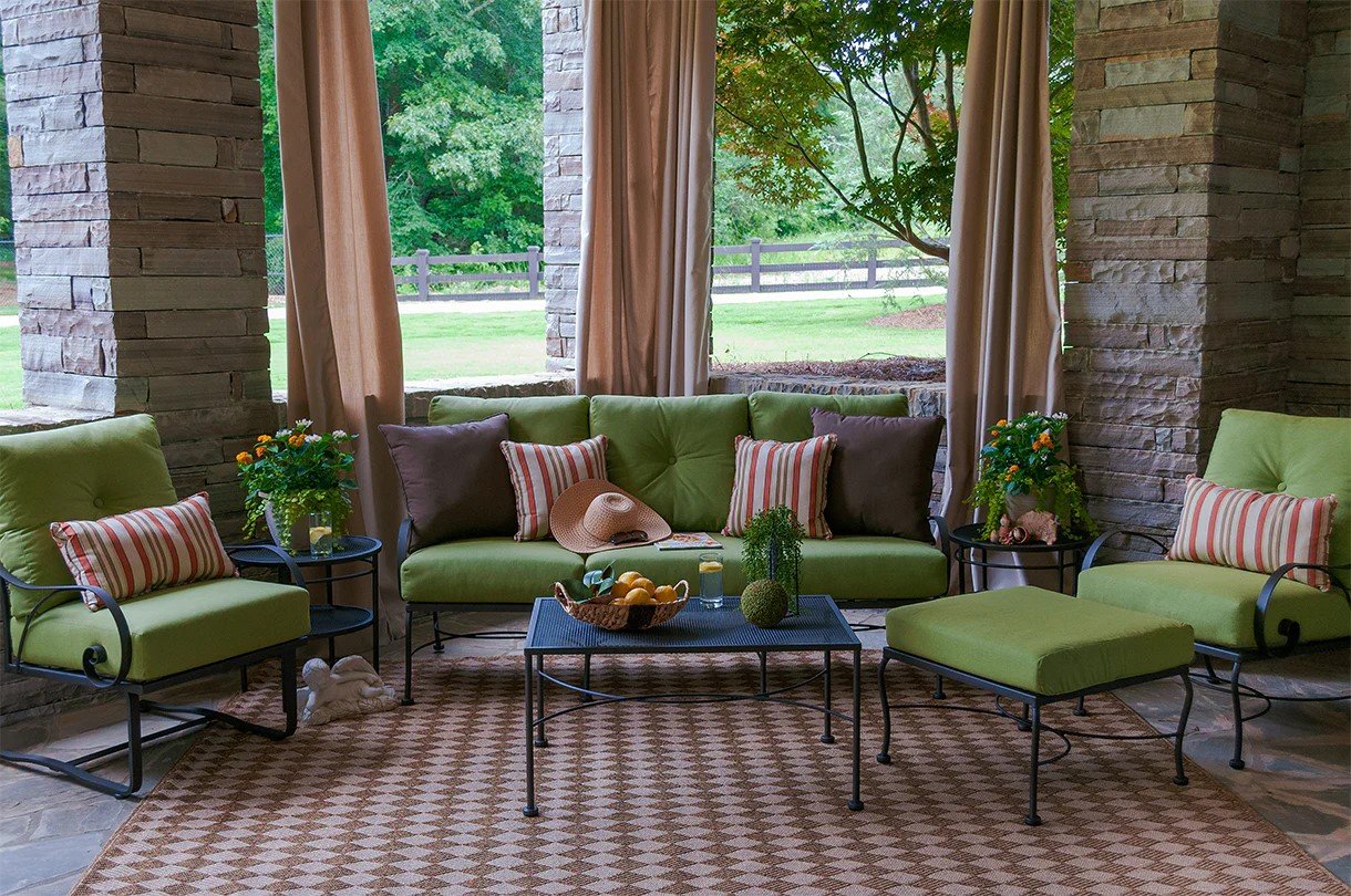 wrought iron lounge set checkered rug next to brick pillars in front of lawn. green cushions on 