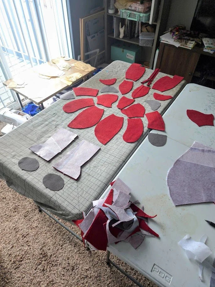 Interior of a living room with craft patterns pieces laid flat on a table, with scraps of fabric next to the fabric pieces.