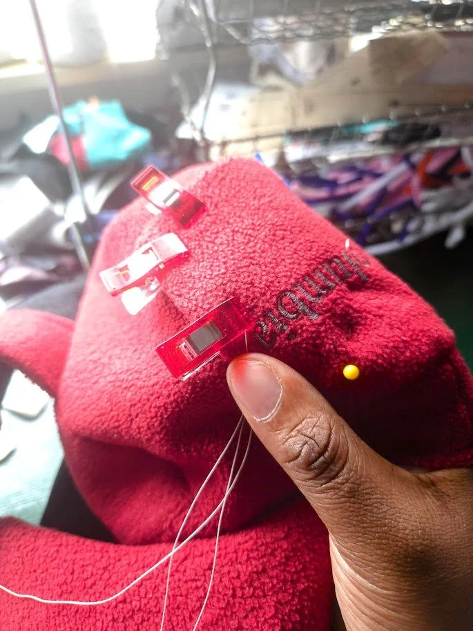 A hand holding a piece of red fleece fabric with a needle and thread.