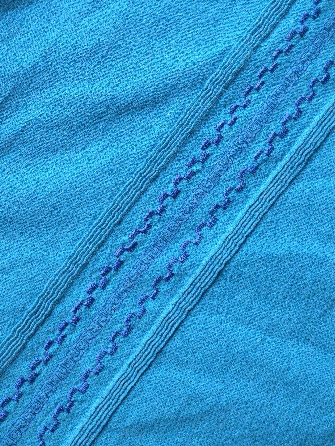 Close up shot of a men's blue collar shirt with pleating and embroidery details.
