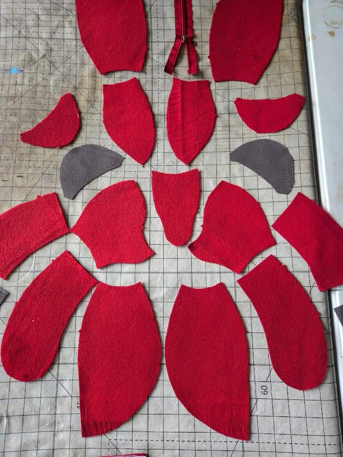 Close-up of craft patterns cut from fabric, forming a red stuffed teddy bear on a table.