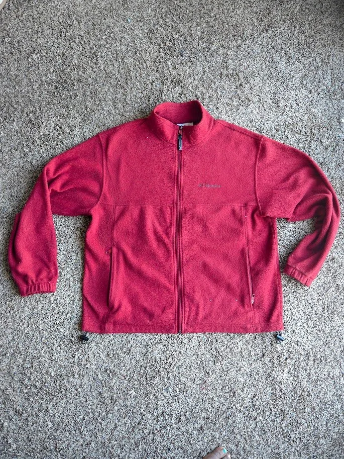 A red Columbia fleece sweater jacket laying flat on a tan carpet.