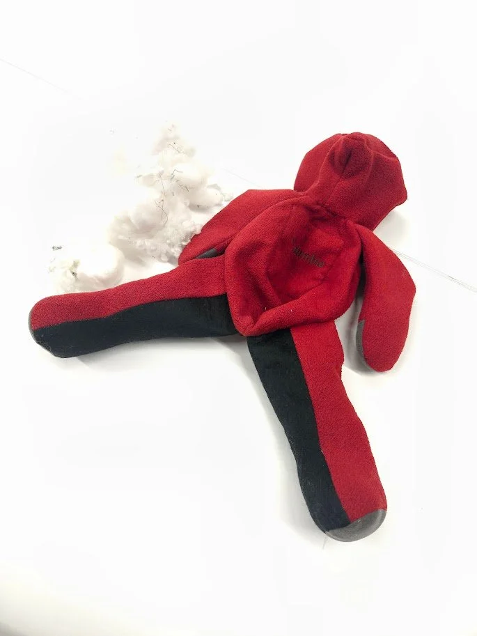 A red and black fleece stuffed teddy bear laying flat on a table, with polyester stuffing next to it.