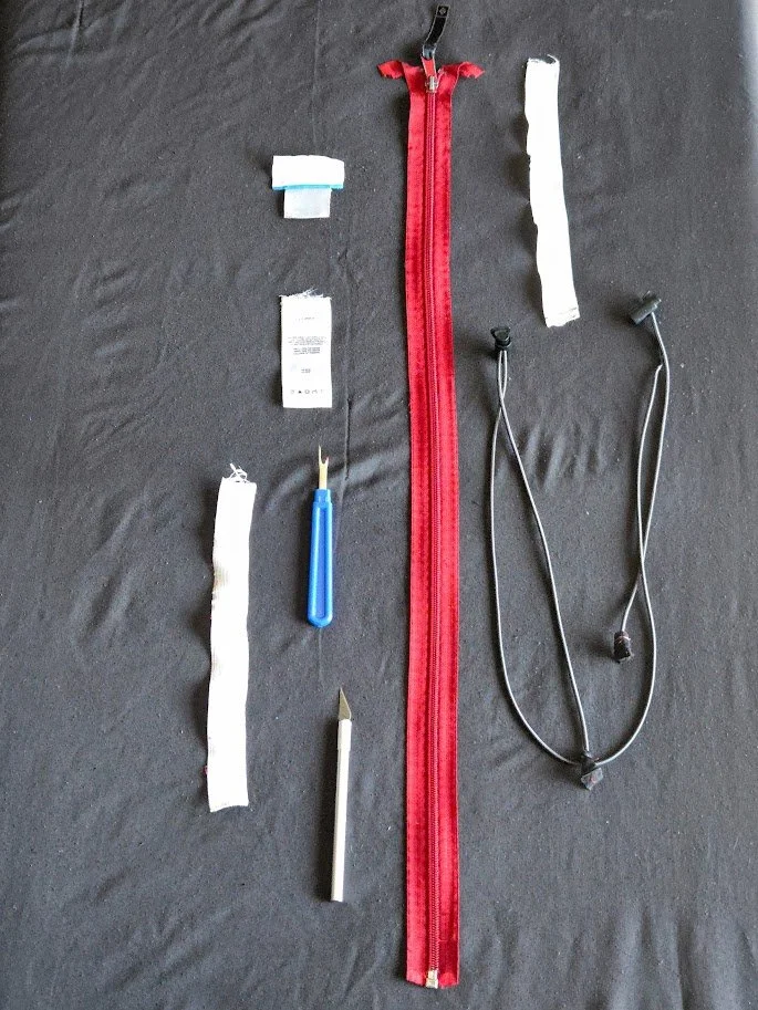 A red zipper, elastic, clothing tags and cutting tools lying flat on a neutral background.