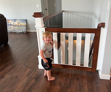 Toddler standing by child safety gate at top of stairs