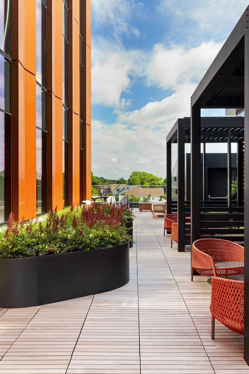 Rooftop amenity deck at 60 Guest Street in Allston featuring modern landscape installation by Xquisite Landscaping. This elevated outdoor space includes sleek wood decking, lush planter beds with ornamental grasses and seasonal color, comfortable lou