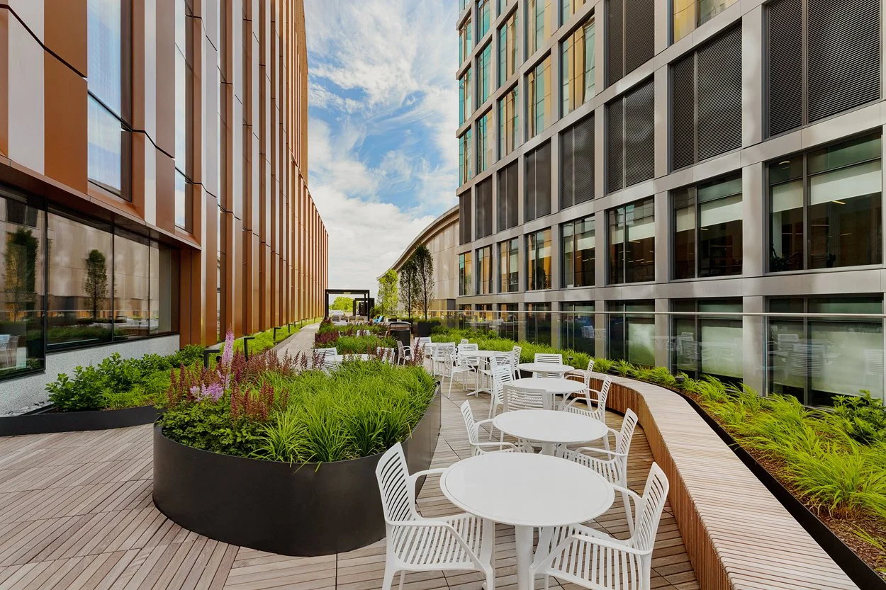 Rooftop amenity deck at 60 Guest Street in Allston featuring modern landscape installation by Xquisite Landscaping. This elevated outdoor space includes sleek wood decking, lush planter beds with ornamental grasses and seasonal color, outdoor cafe se