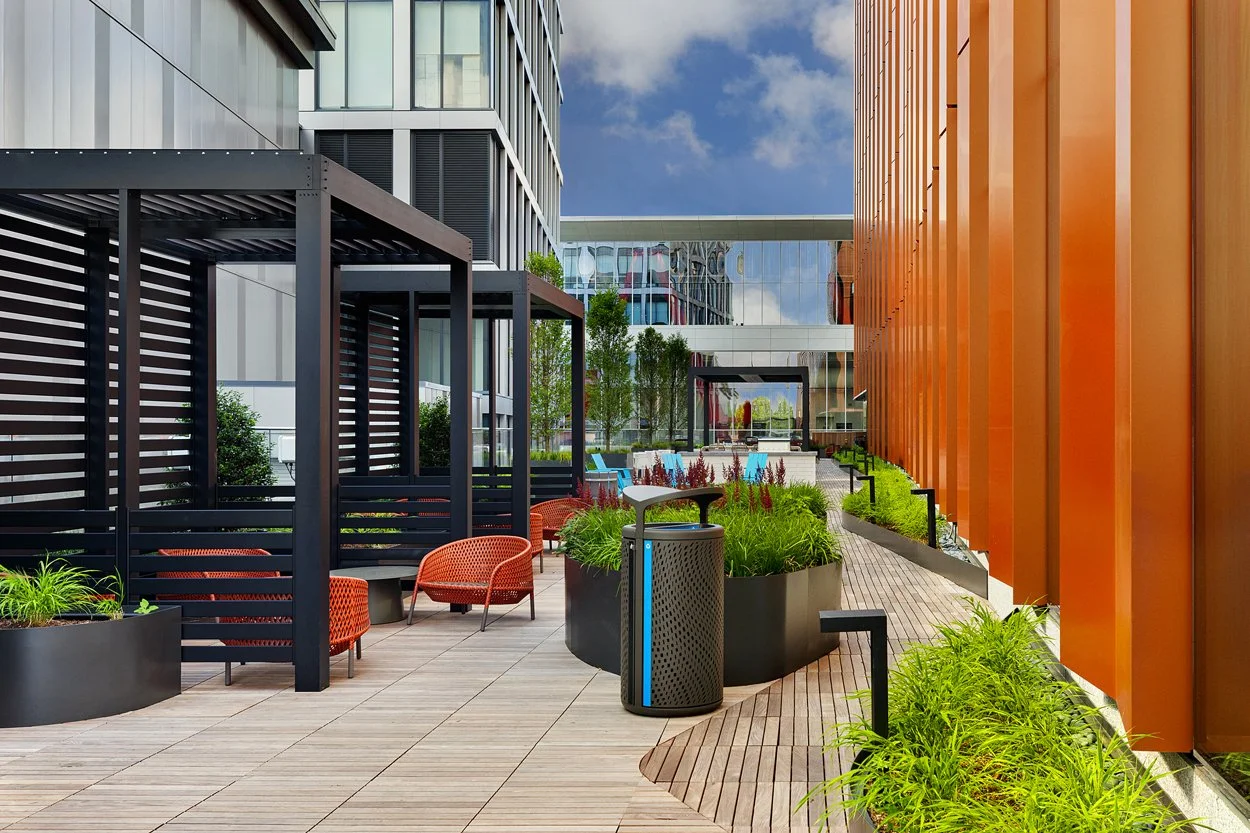 Rooftop amenity deck at 60 Guest Street in Allston featuring modern landscape installation by Xquisite Landscaping. This elevated outdoor space includes sleek wood decking, lush planter beds with ornamental grasses and seasonal color, comfortable lou