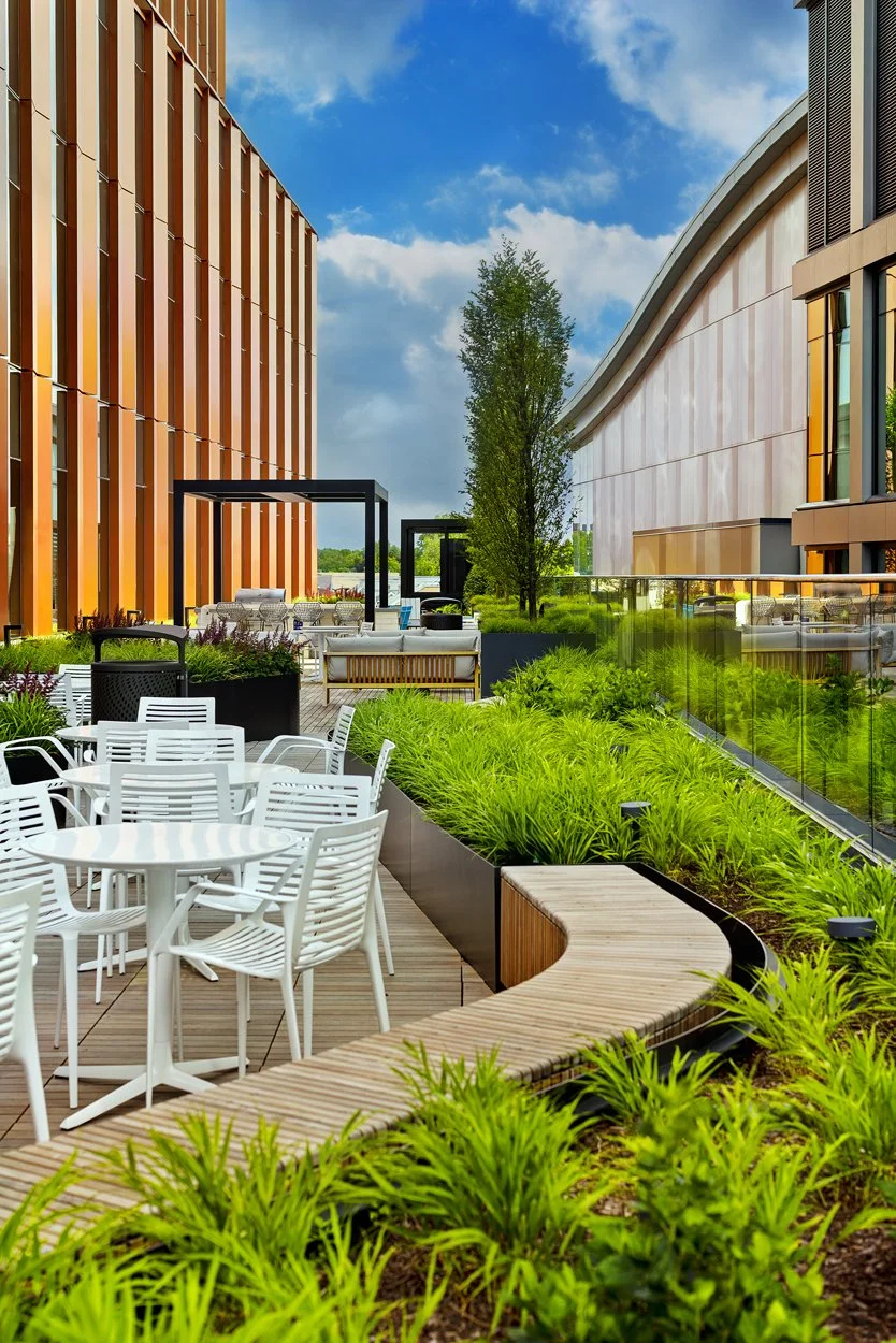 Rooftop amenity deck at 60 Guest Street in Allston featuring modern landscape installation by Xquisite Landscaping. This elevated outdoor space includes sleek wood decking, lush planter beds with ornamental grasses and seasonal color, outdoor cafe se