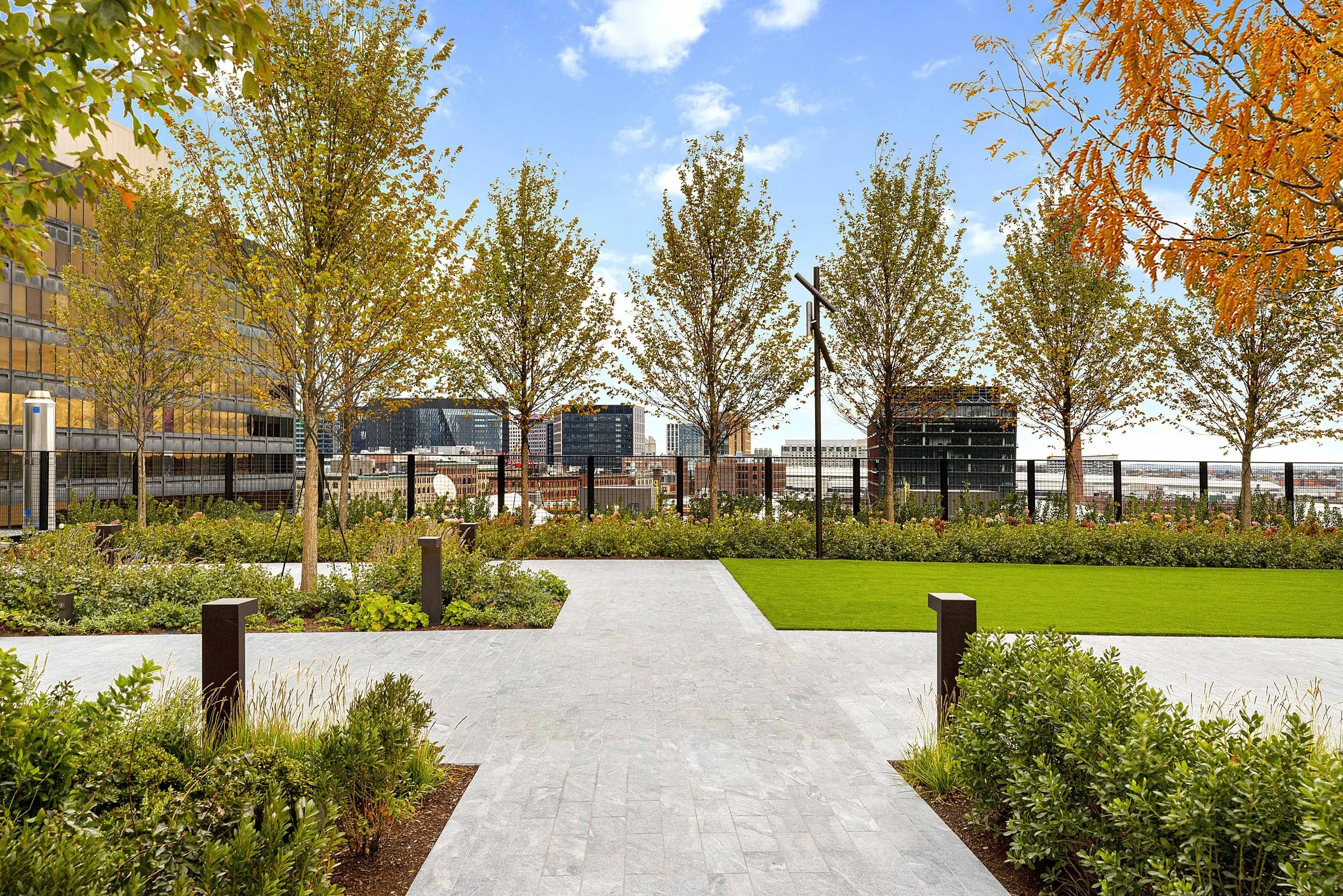 Detail of the intersection of granite paths at the 11th floor Sky Park at the new South Station Tower in Boston. A variety of trees and ground shrubs and flowers are visible. High performance artificial turf is in one section.