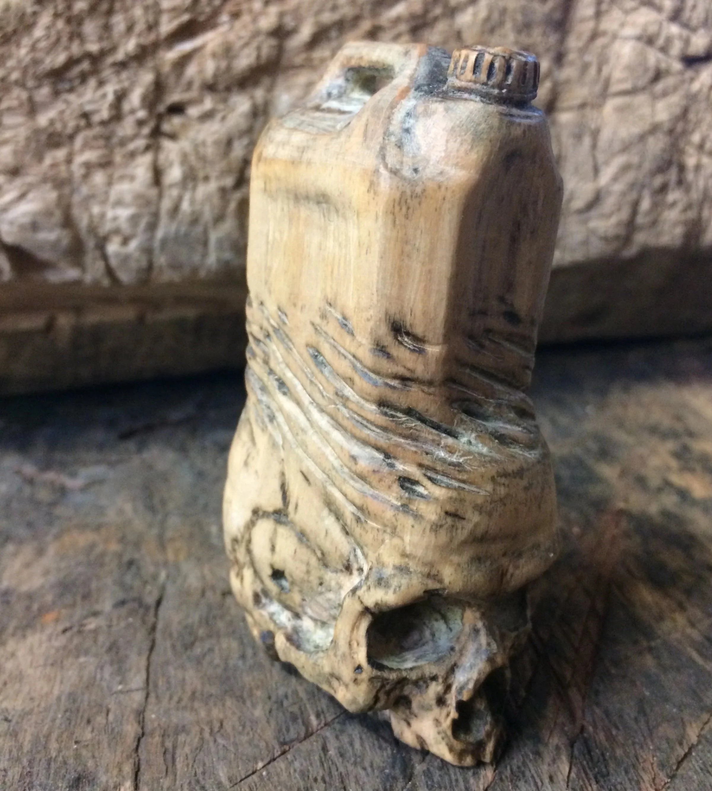 A plastic container morphs into a skull hand carved miniature sculpture in holly timber by Jason Thomson