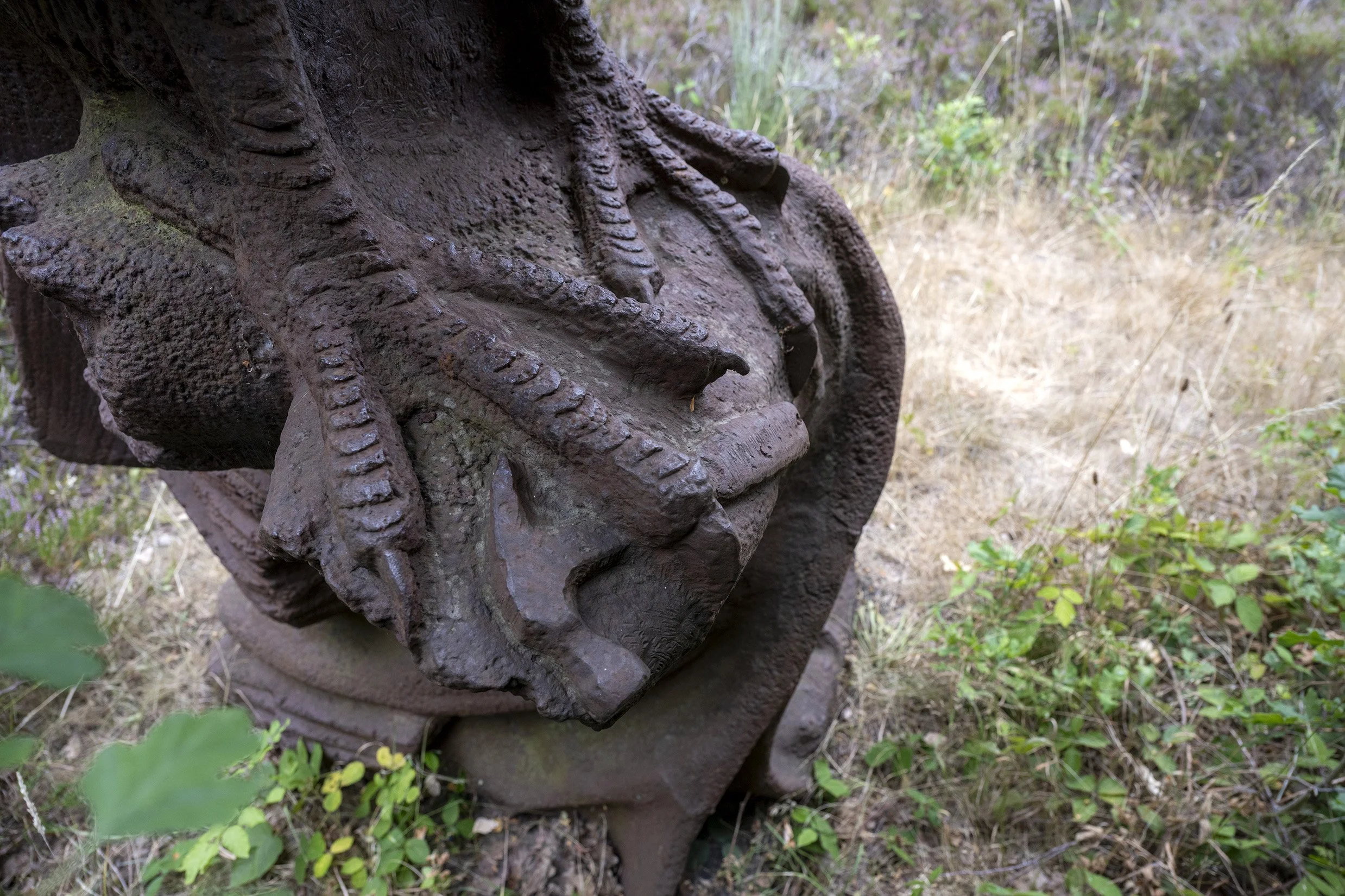 A Stanley claw hammer is held by a giant bird of prey's talons on top of a weathered tree stump. Iron Sculpture detail of The Bird and the Boy by Jason Thomson. Sculpture in nature.