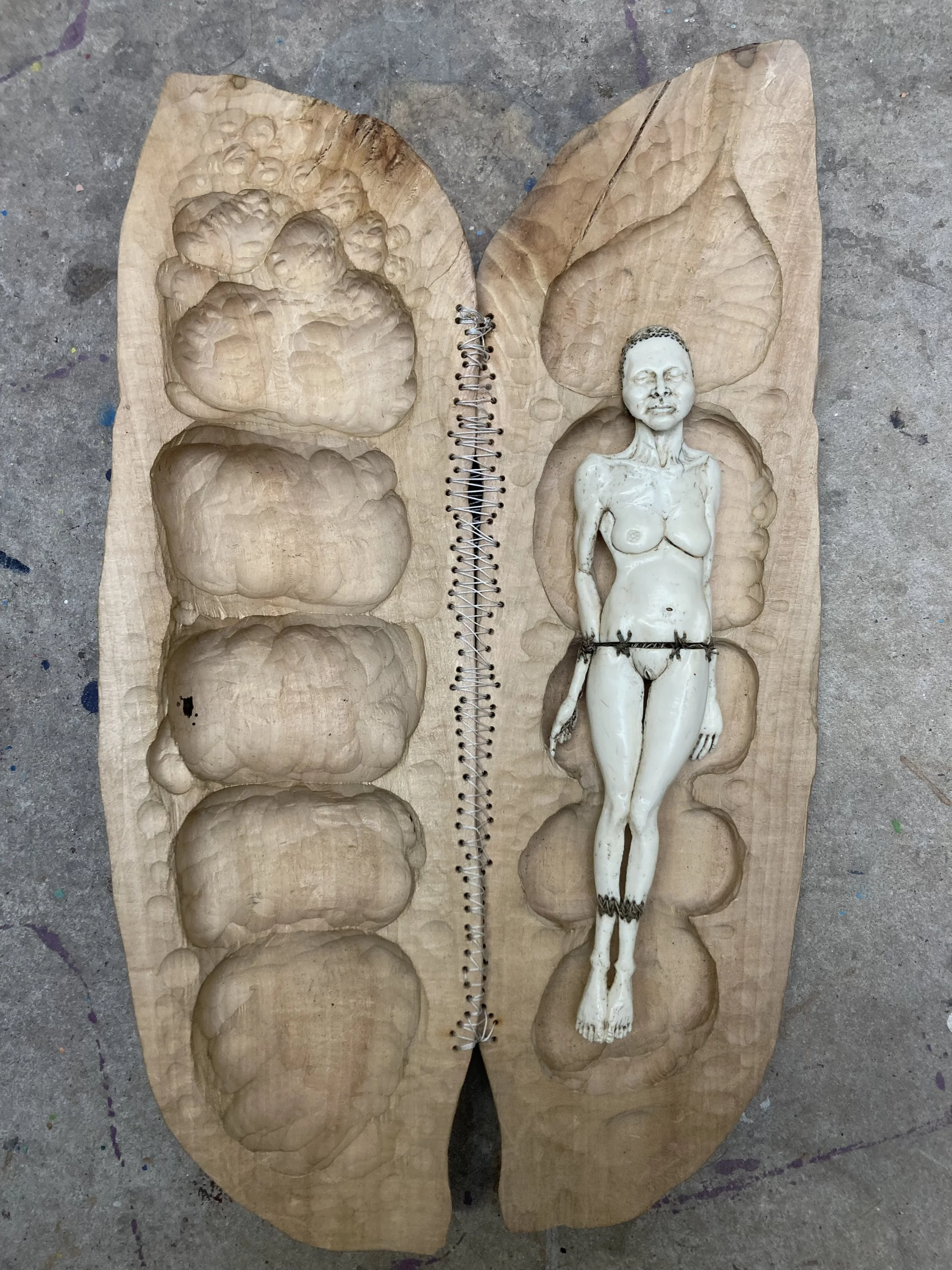 A  hand carved lime wood pea pod capsule, stitch hinged, open to reveal carved bone miniature stitched hand carved woman mother figure grave goods by Jason Thomson