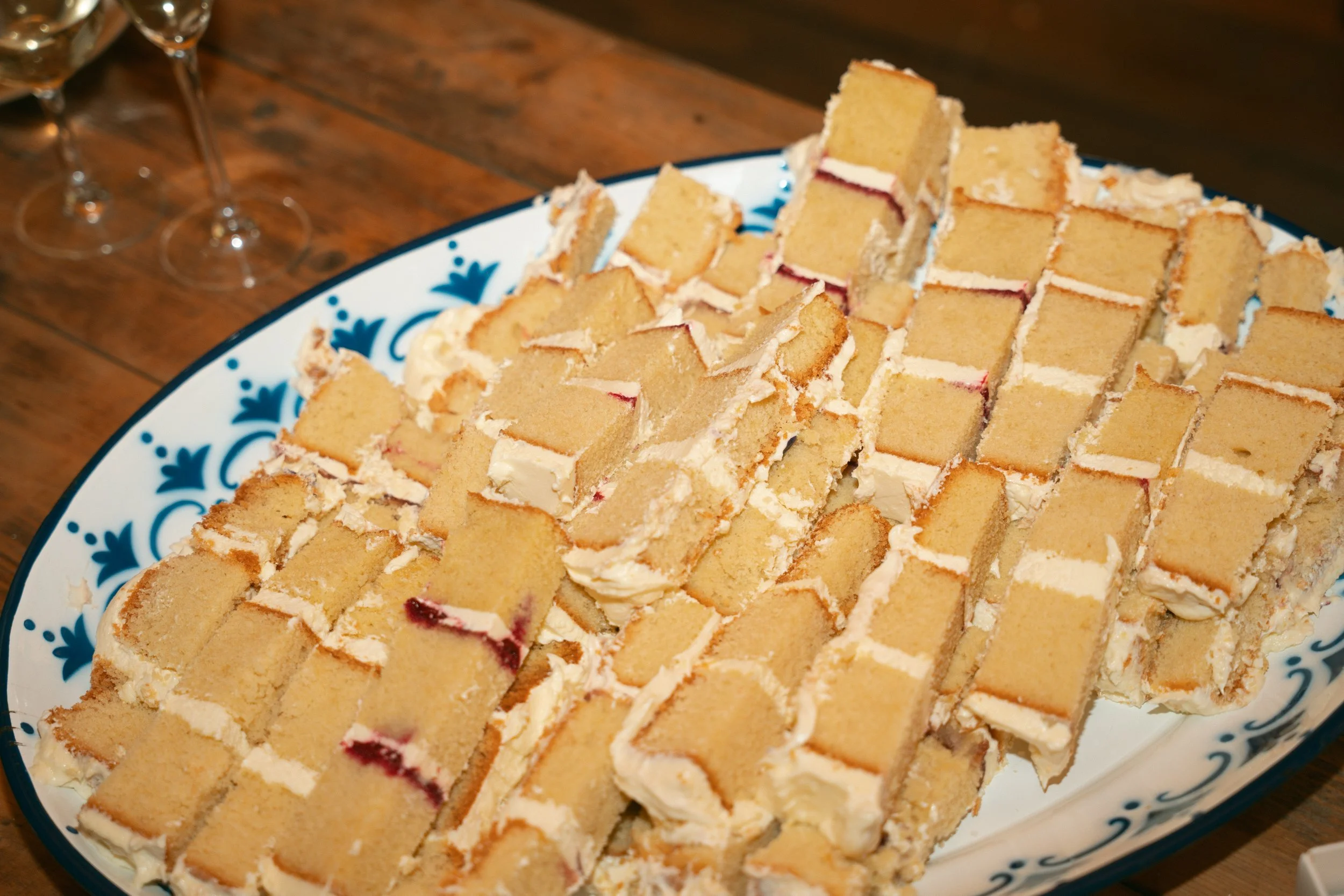 A large platter of sliced yellow cake with white frosting and red jam filling, set on a wooden table.