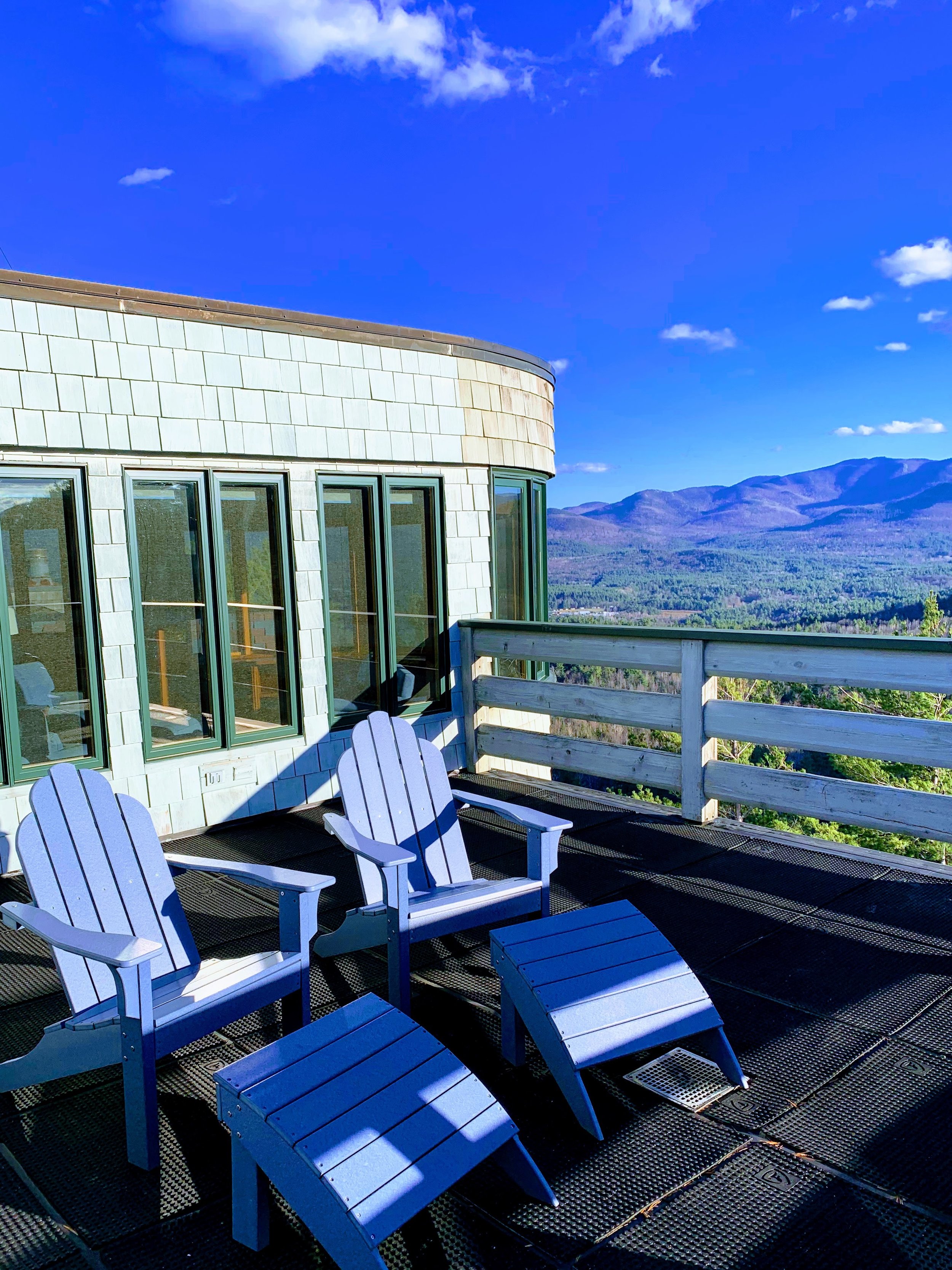 Mountain view with Adirondack chairs on a deck next to a modern building with large windows.
