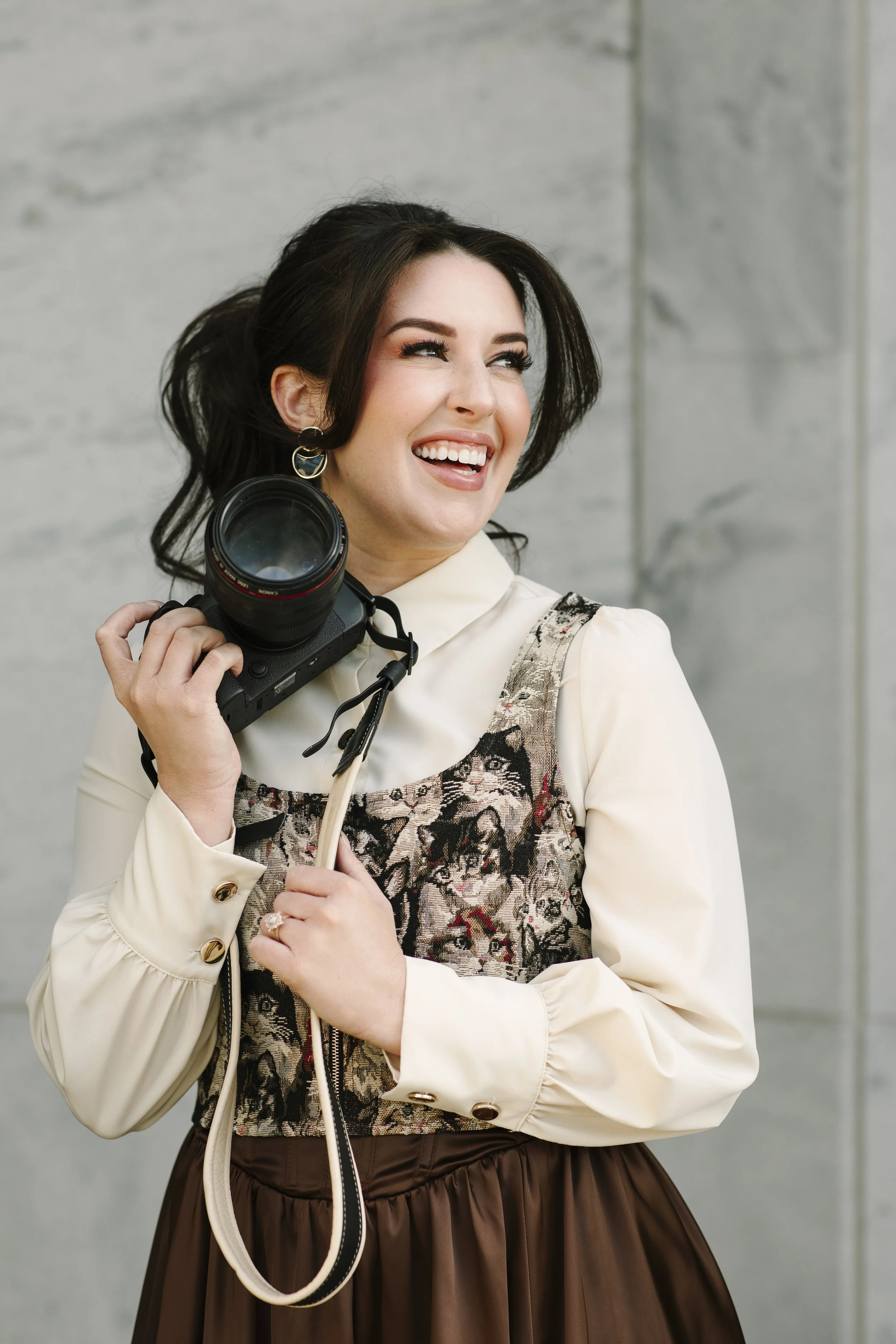 Smiling woman in a white blouse and patterned dress holding a DSLR camera