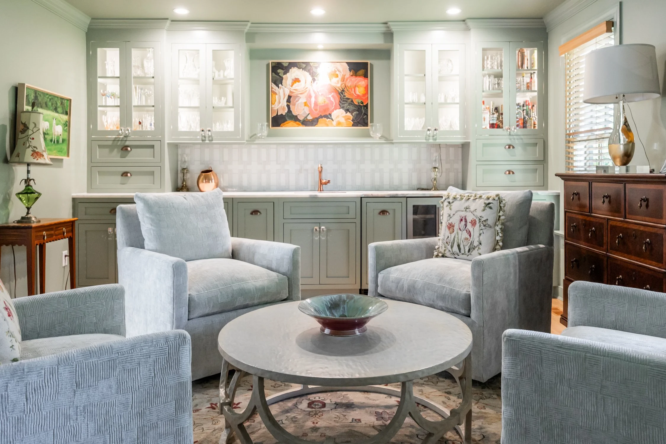 Four upholstered swivel chairs arranged around a round coffee table in a living room with built-in cabinetry and wet bar.