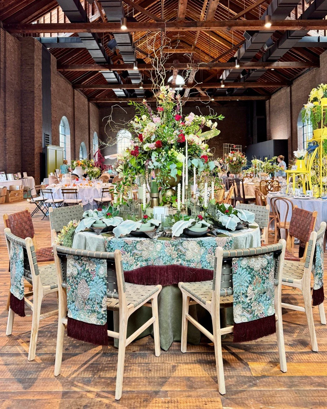 Full view of a tablescape titled A Garden Beyond Time, featuring layered green linens, chair pennants, a lush floral centerpiece, and coordinated tableware and accessories.