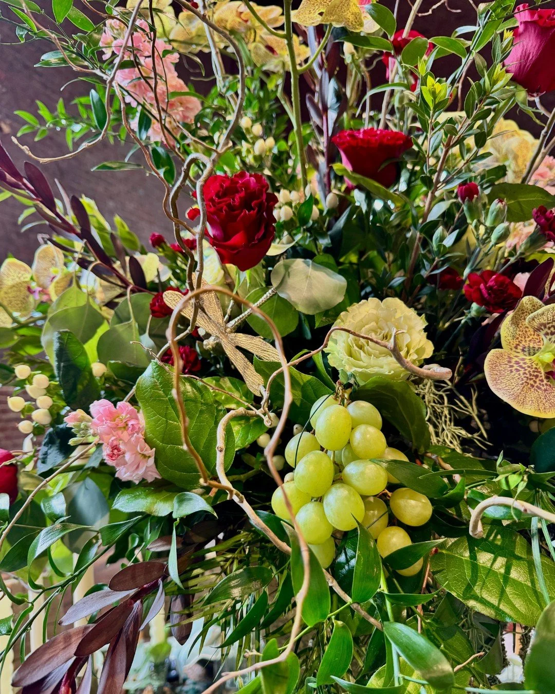 Close-up of a lush floral centerpiece featuring roses, berries, greenery, curly willow, and phalaenopsis orchids in a rich, layered arrangement.