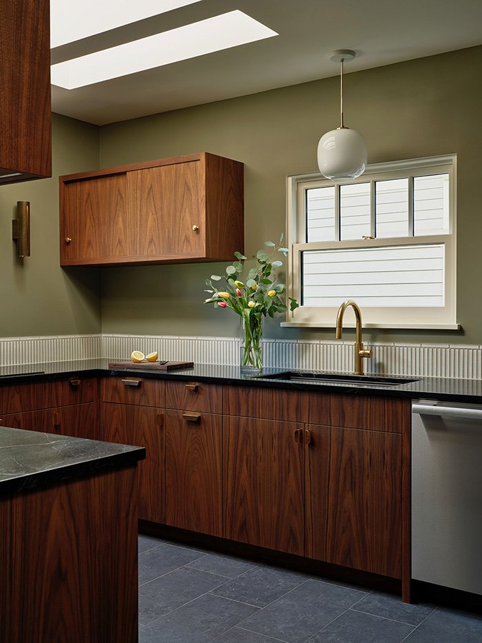 A wide angle view of a remodeled kitchen. There are walnut cabinets, tiled floor, and skylights. 