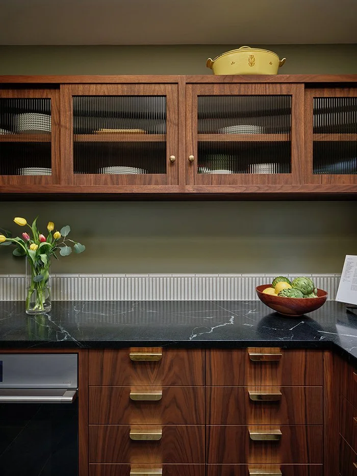 A kitchen with walnut cabinetry and drawers, green walls, and soapstone counter. 