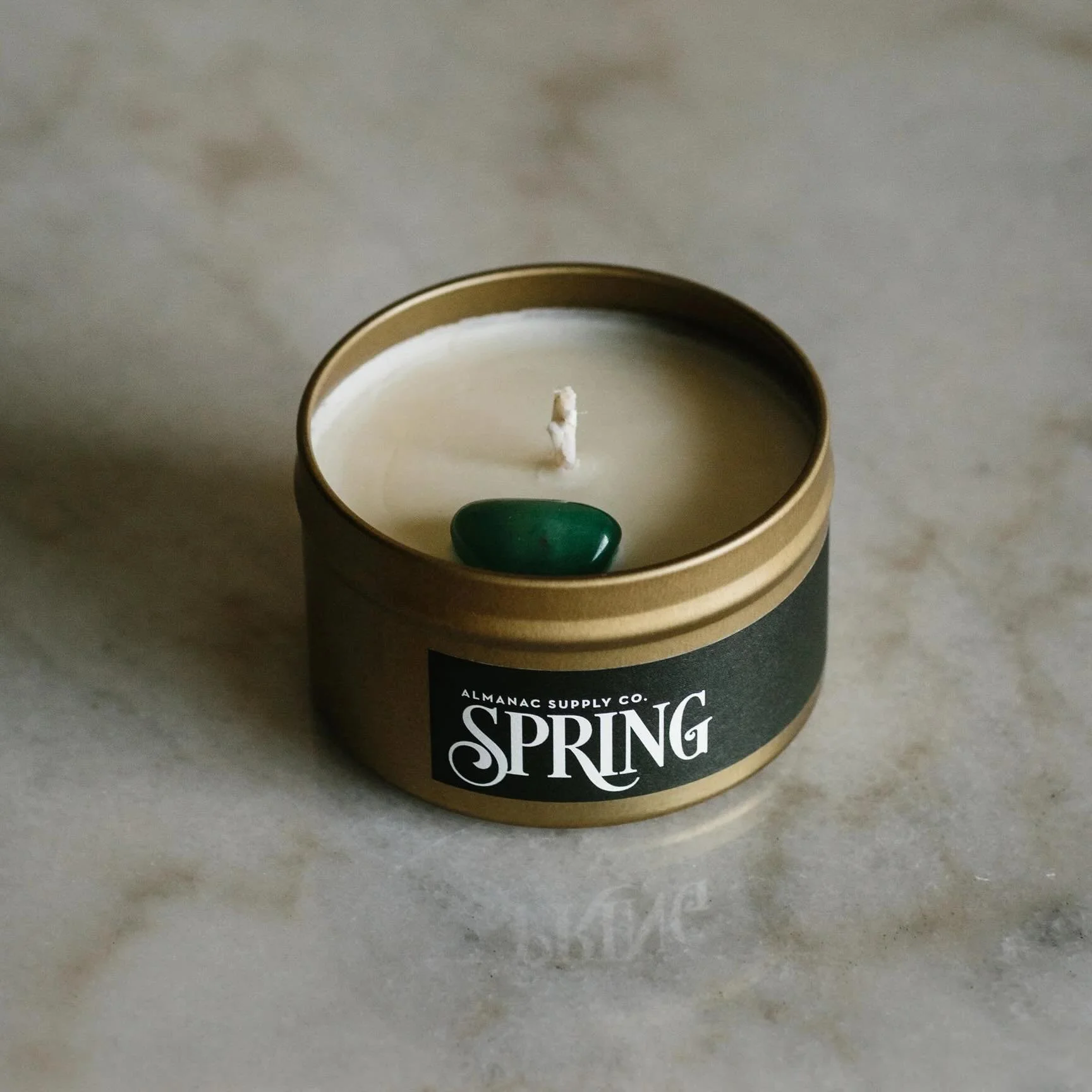 Almanac Supply Co candle in gold tin with green stone