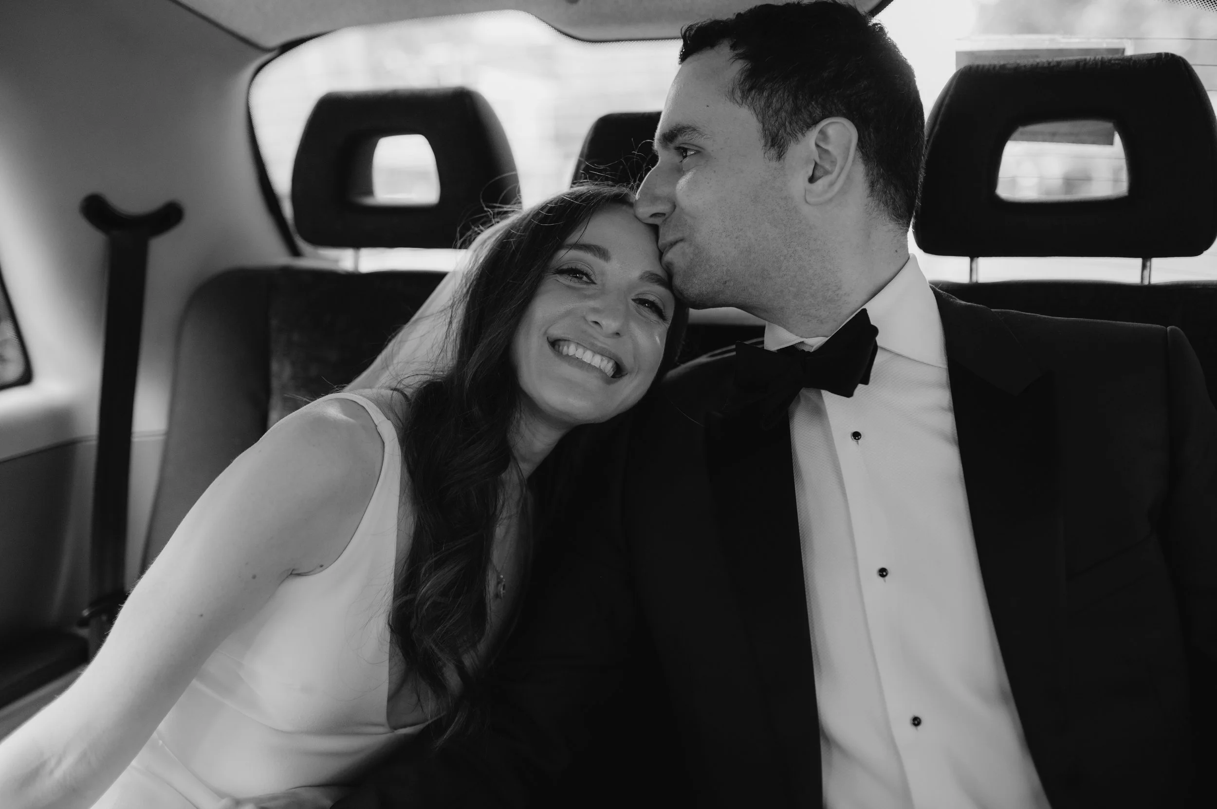 London wedding photography at Marylebone Town Hall groom kissing bride on top of head in back of taxi