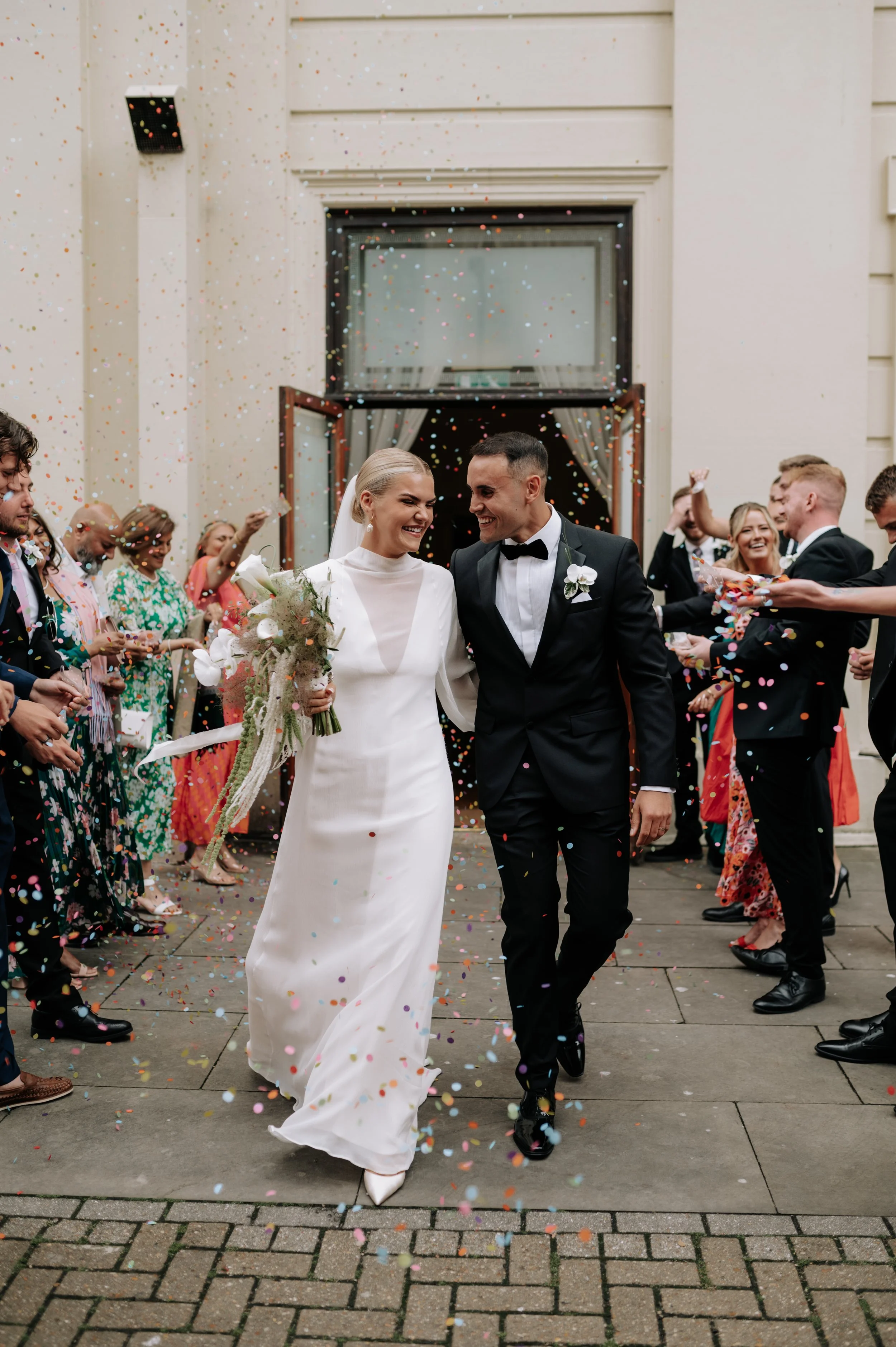 Bride and groom walking through colourful confetti at Brighton wedding. Fine art documentary wedding photography. 